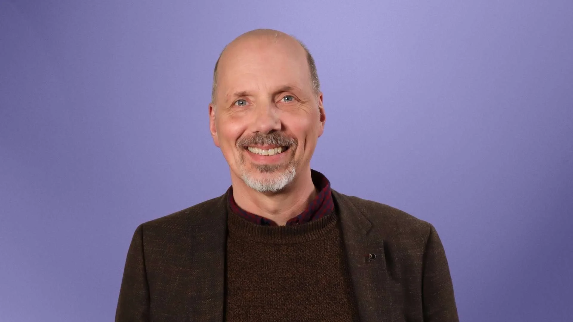 Kjartan brosandi í dökkum fötum með fjólubláan bakgrunn