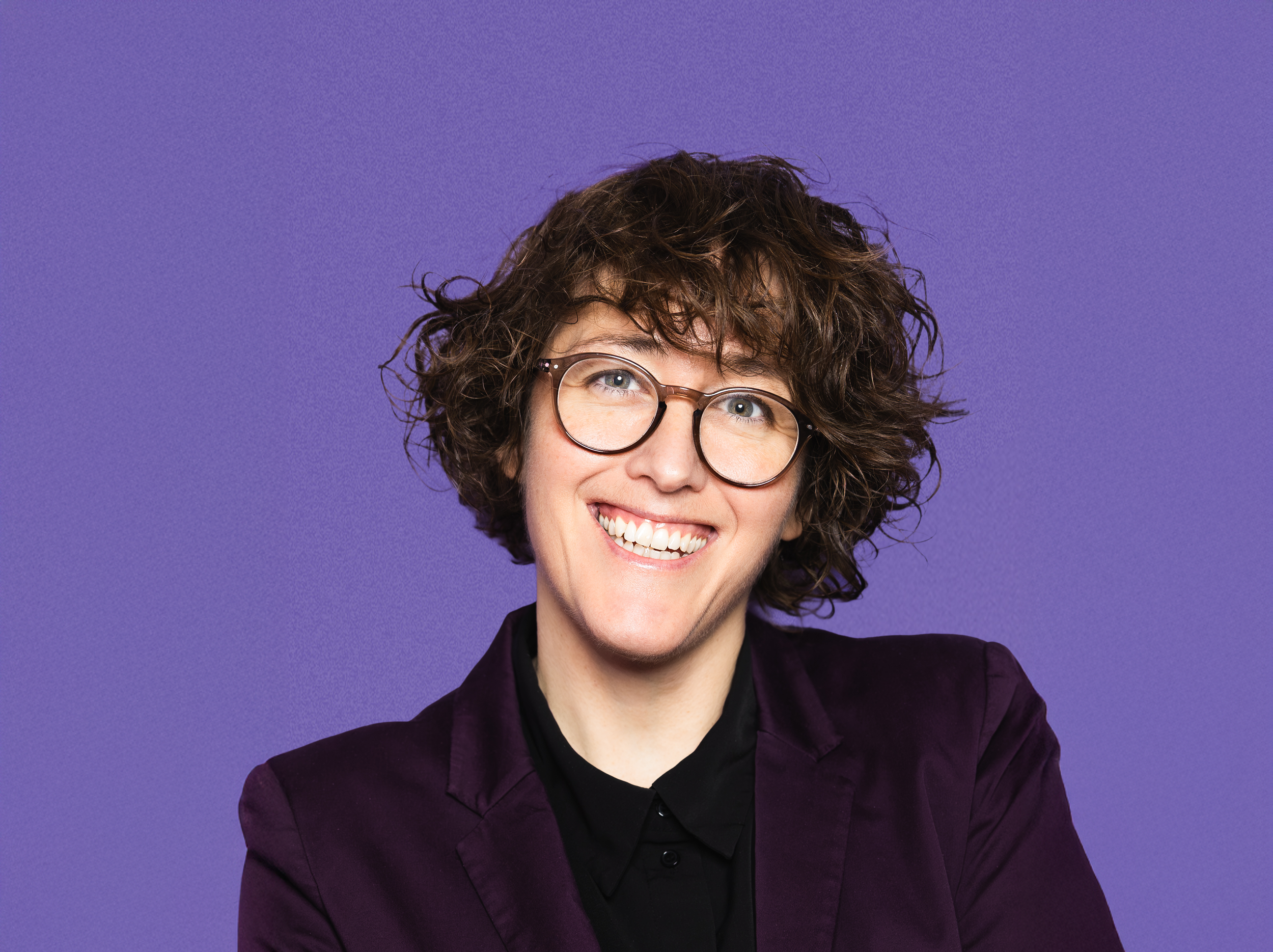 Oktavía með brúnt ótamið hár og létt bros á ljósum bakgrunni með myndum á vegg