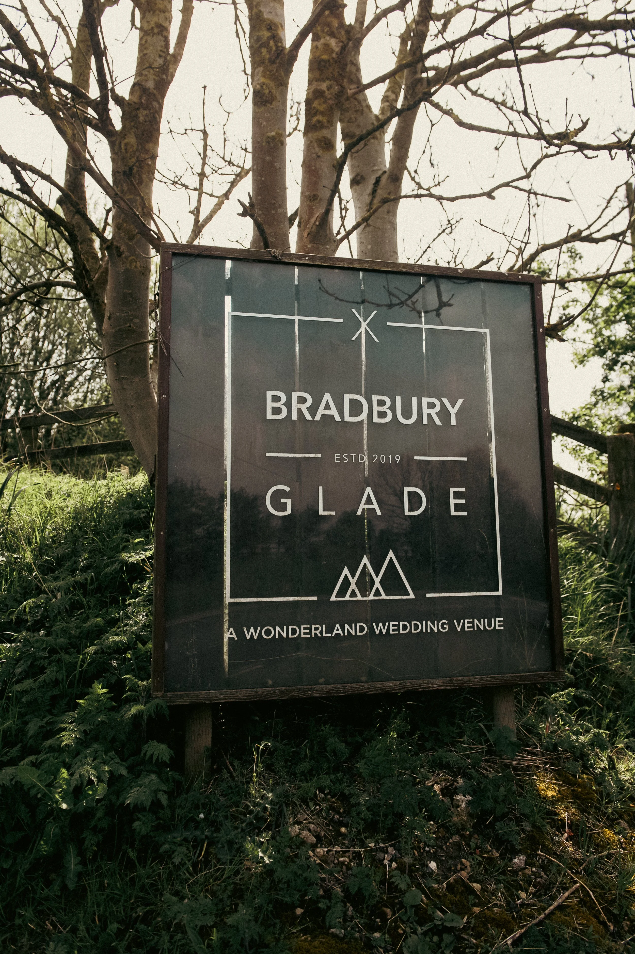 Signboard for Bradbury Glade, a wedding venue established in 2019, located outdoors with trees and greenery around.