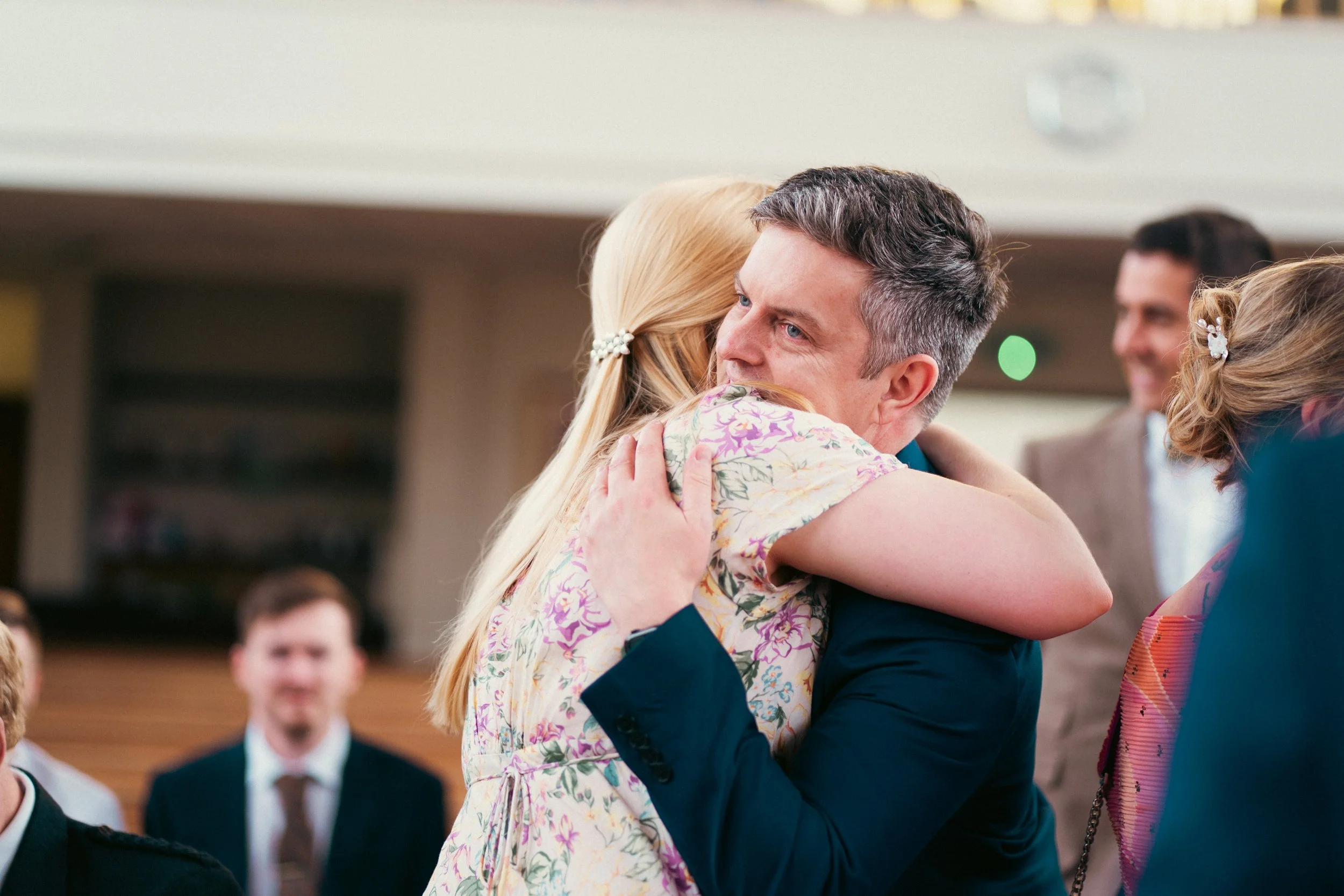 A man and woman hugging, with other people in the background at what appears to be a social or celebratory event.