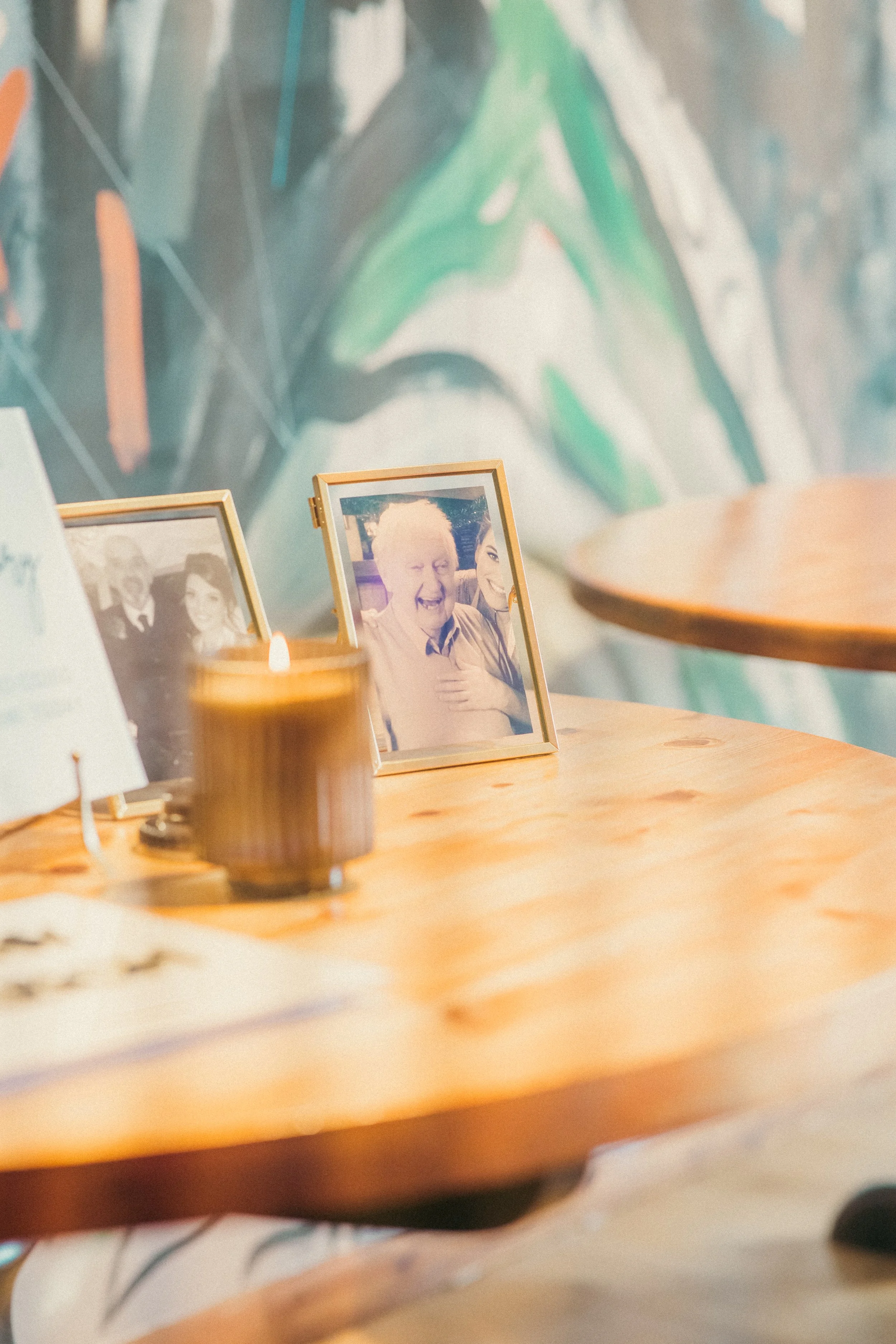 A wooden table with framed photographs, a burning candle, and a blurred background with colorful mural art.
