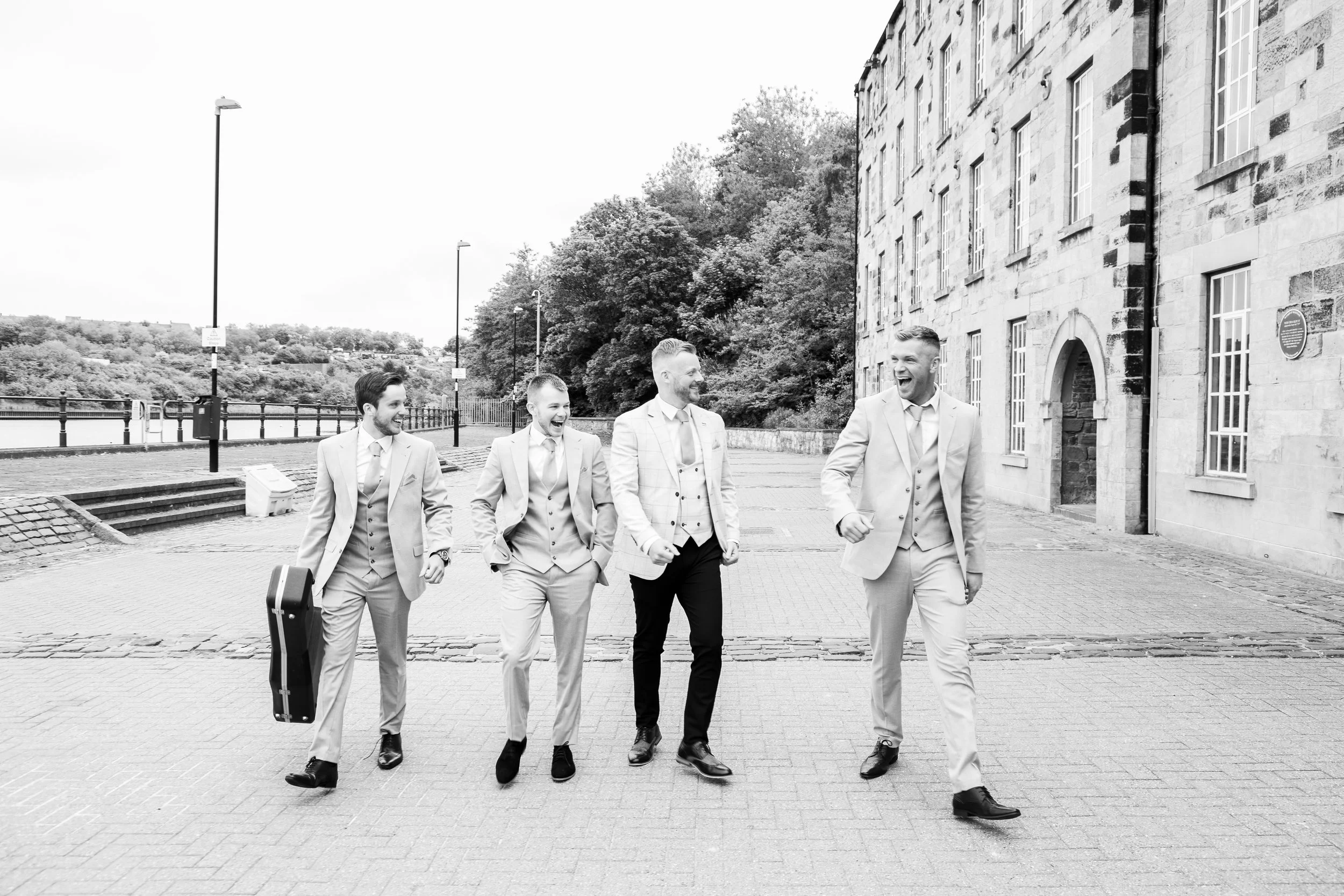 Five men dressed in suits walking outdoors, smiling and talking to each other.