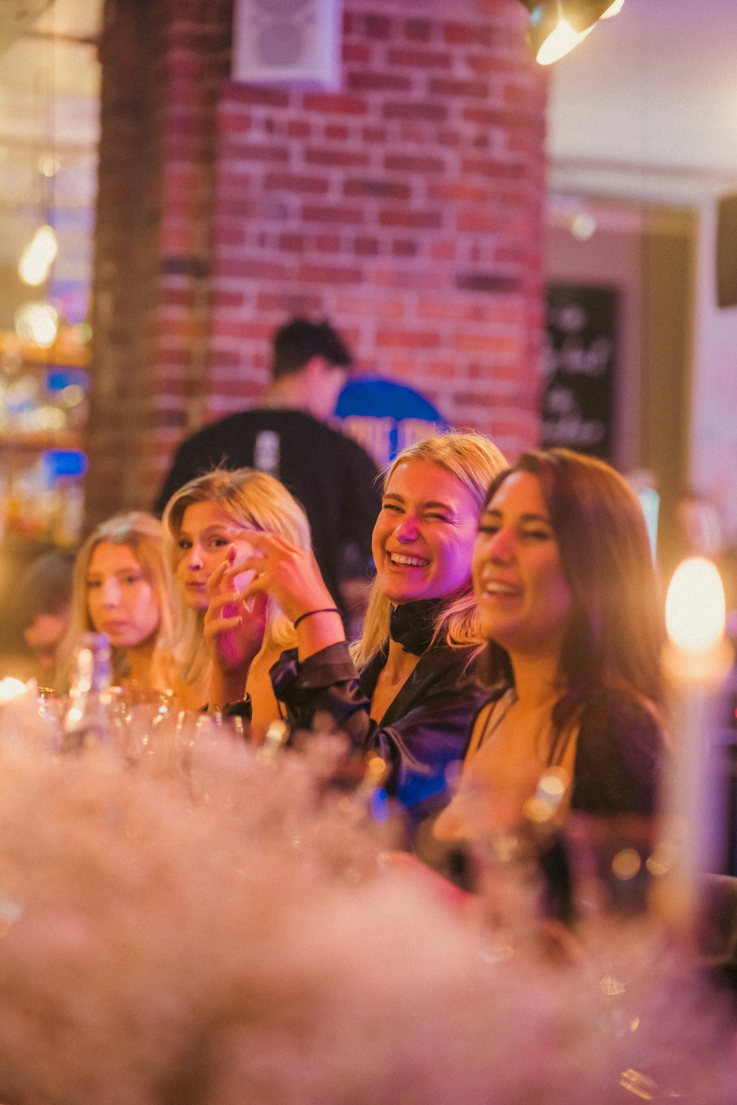 A group of people enjoying themselves at a restaurant or bar, with a brick wall in the background and warm lighting.