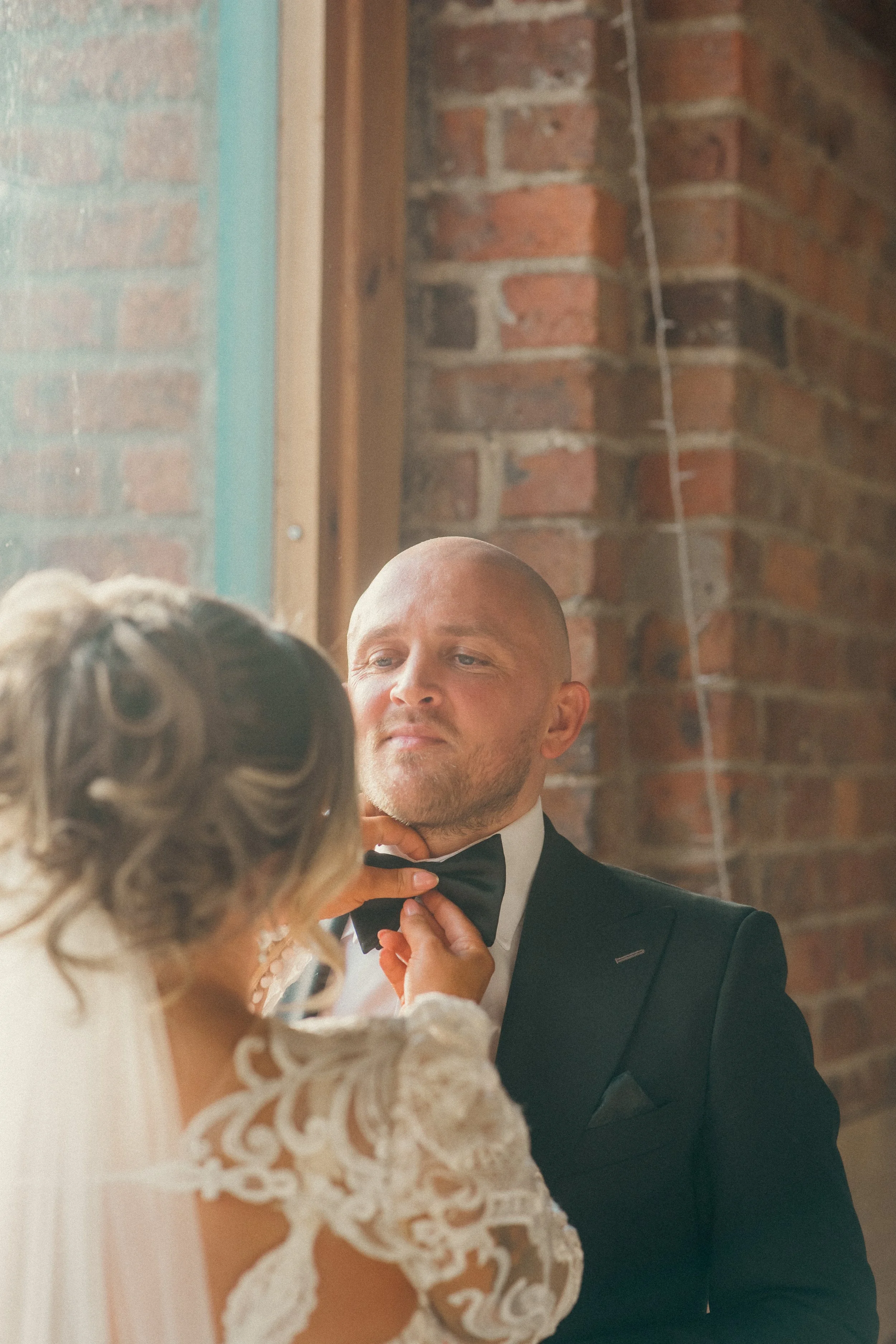 Woman in wedding dress adjusting a man's black tuxedo bow tie during a wedding.