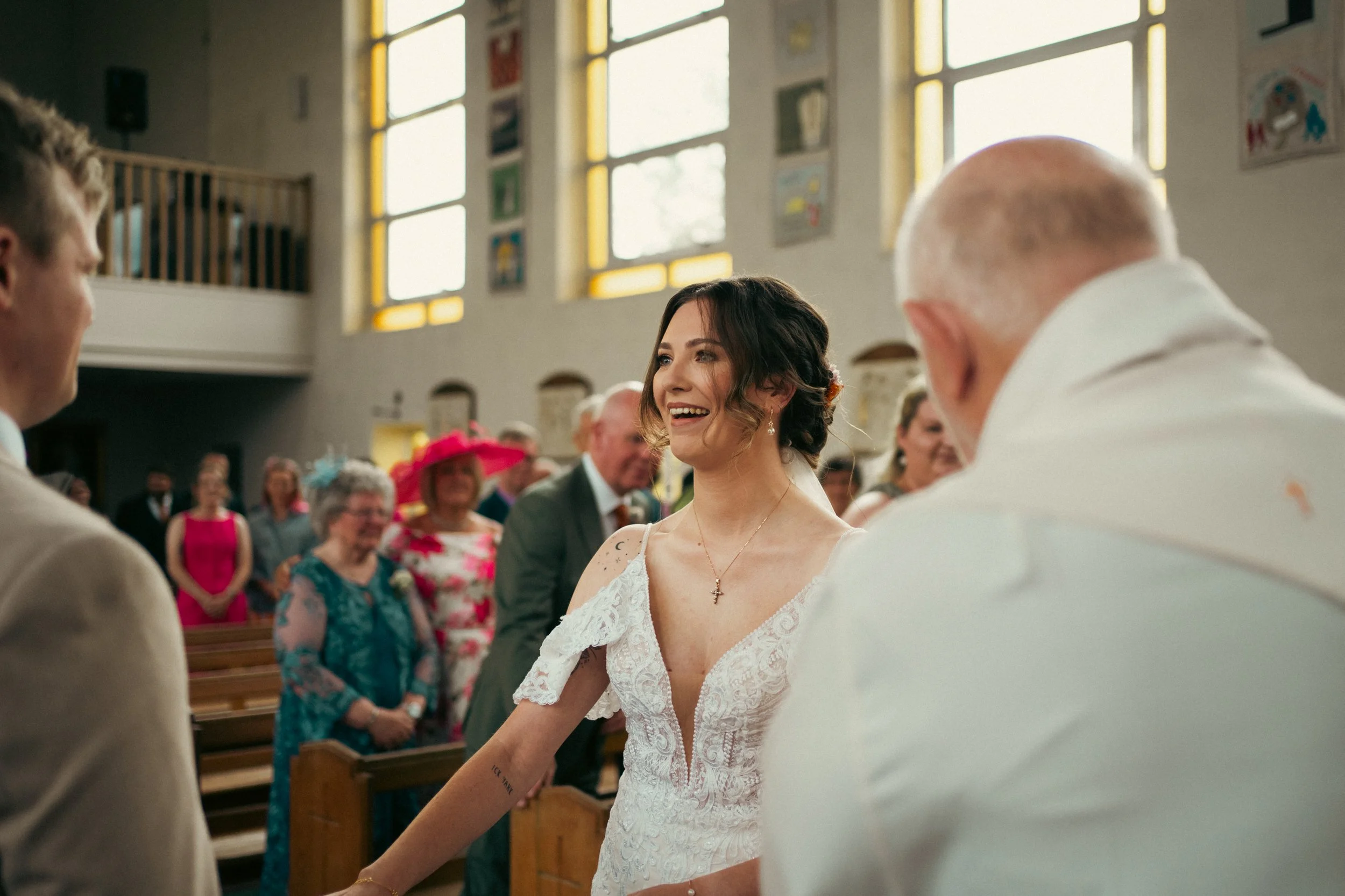 A bride smiling during a wedding ceremony inside a church with guests in the background.