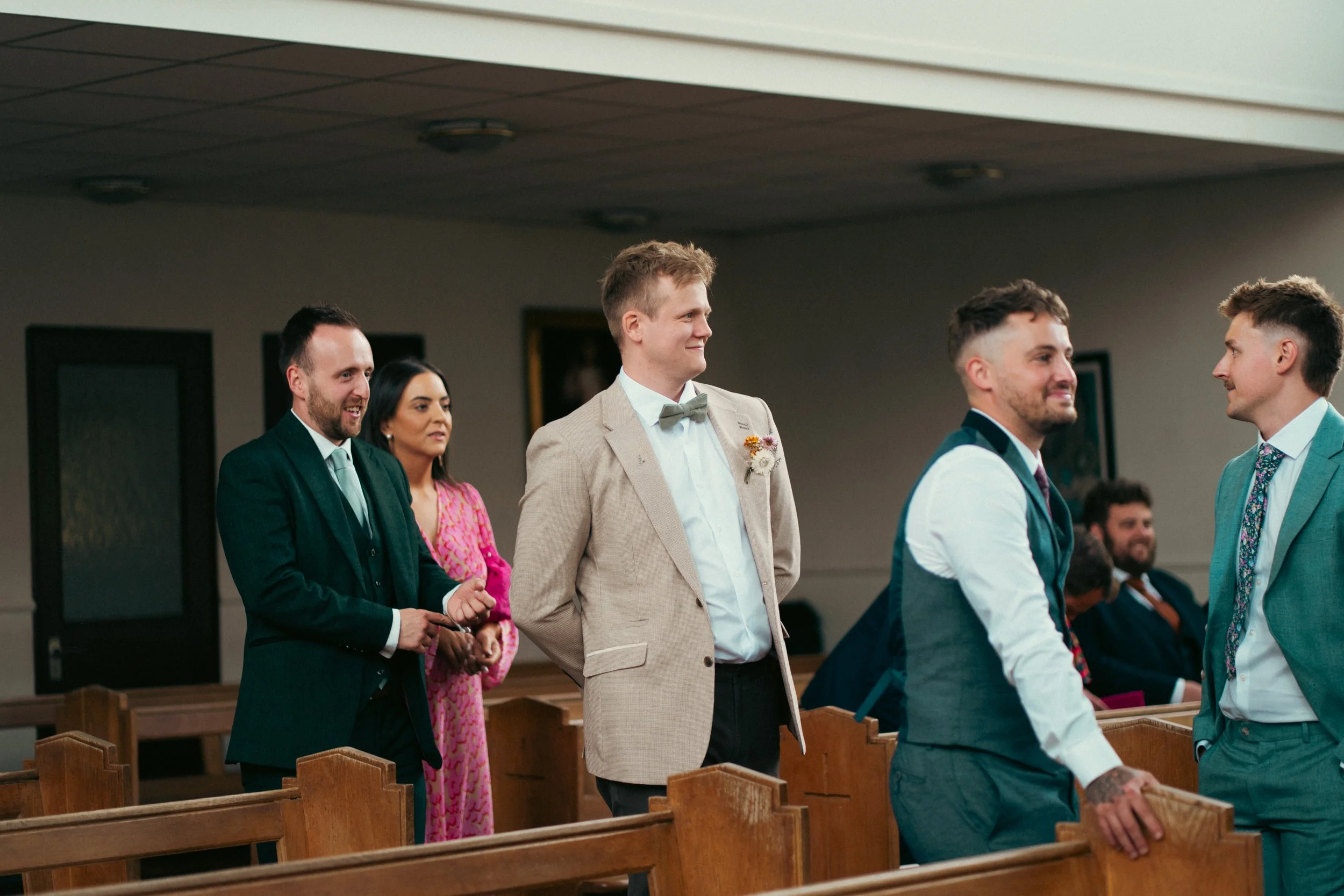 People standing in church pews during a wedding ceremony, exchanging vows, with a mix of formal and semi-formal attire.