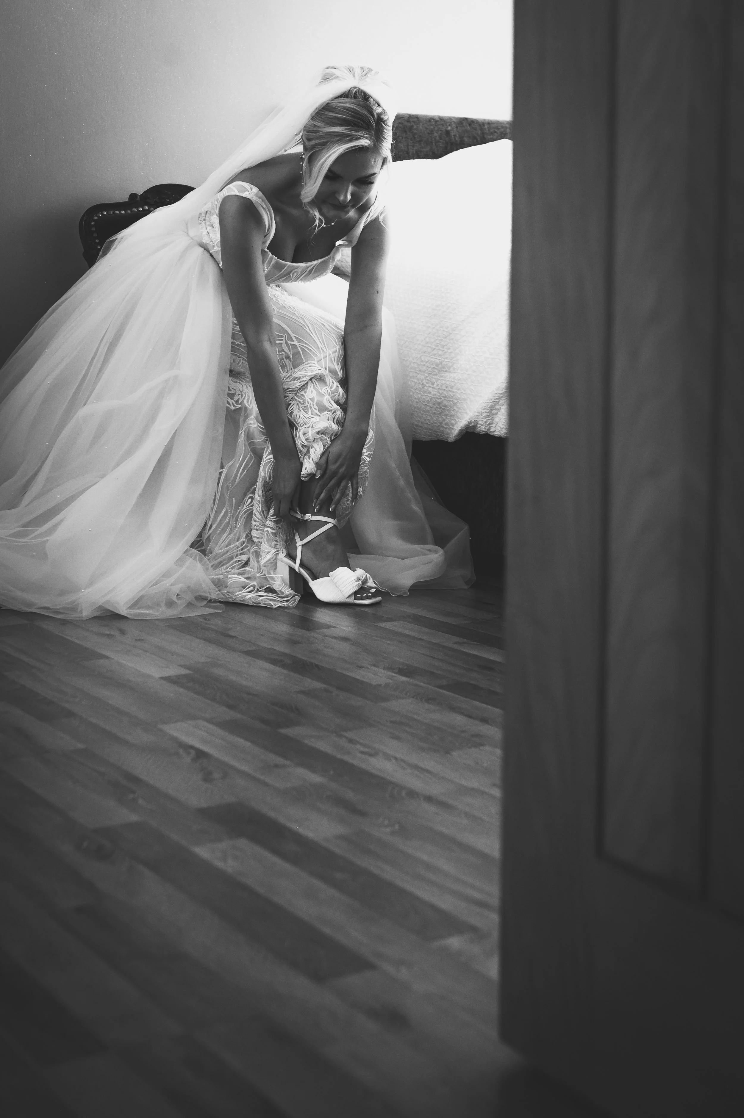 Bride in wedding dress putting on her shoe on the bedroom floor.