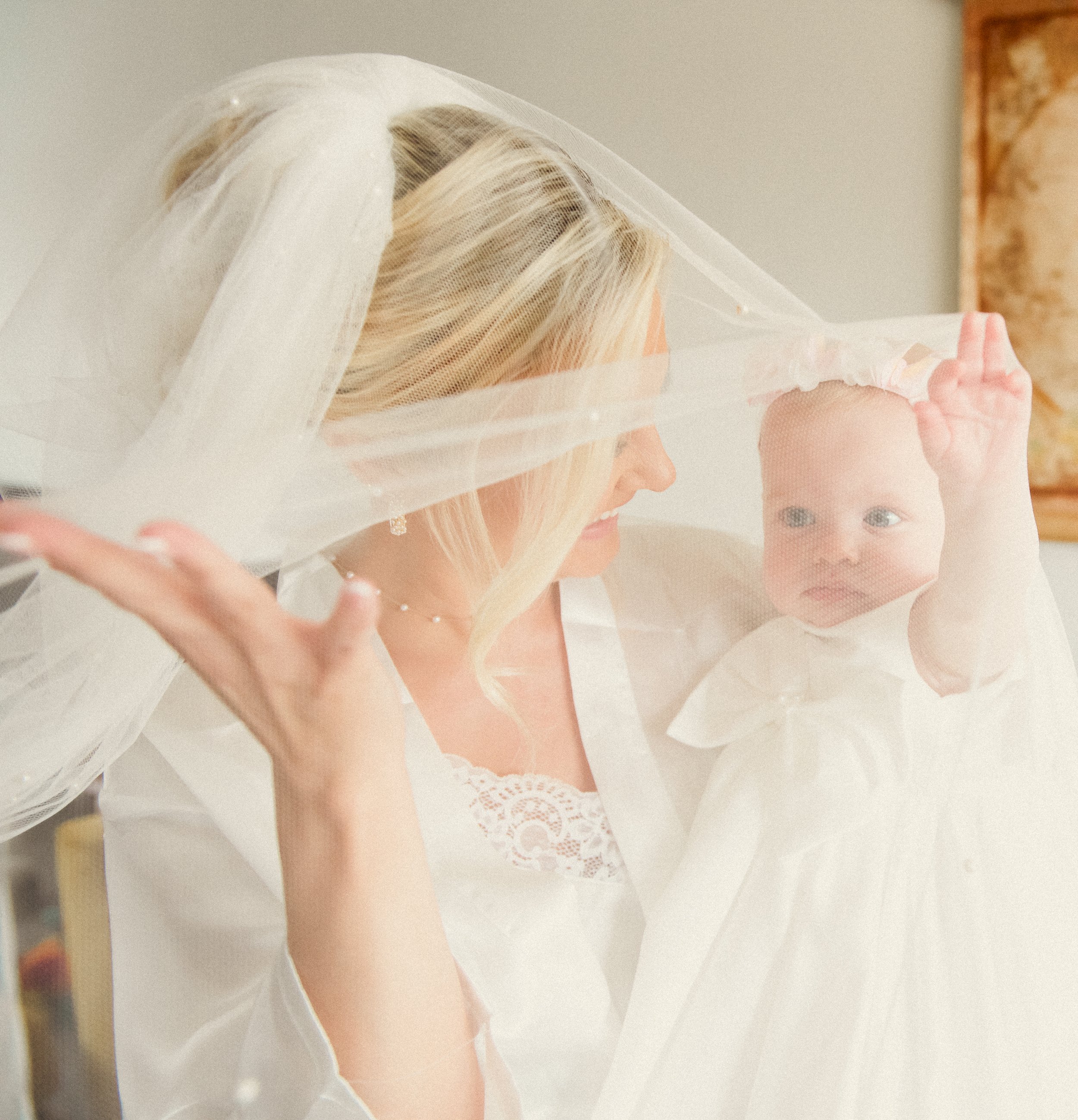 A woman and a baby are playing with a sheer veil. The woman is smiling, and the baby is reaching up with one hand while looking at the veil.
