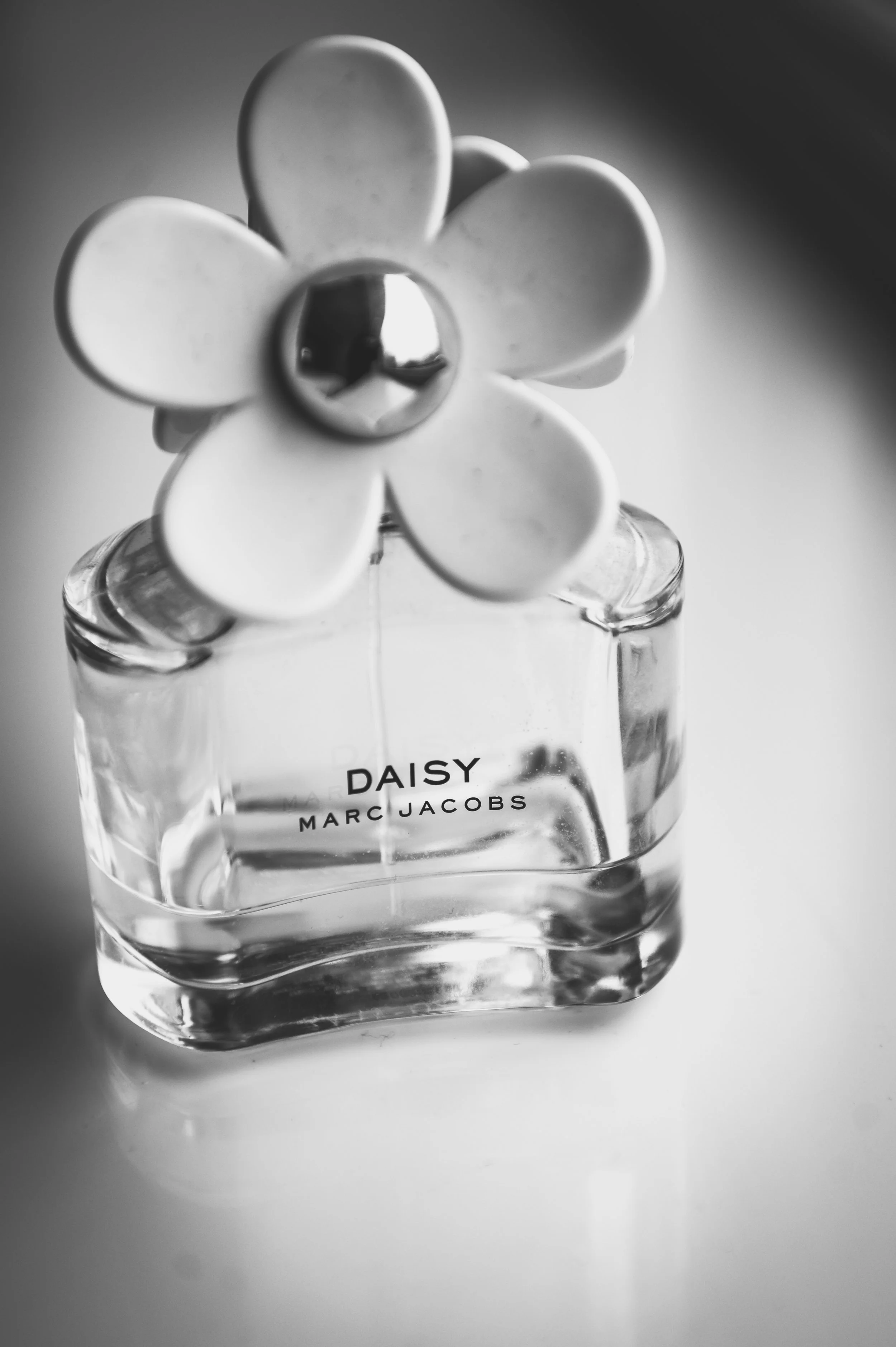 A glass perfume bottle labeled 'Daisy' by Marc Jacobs, topped with a flower-shaped cap, in black and white.