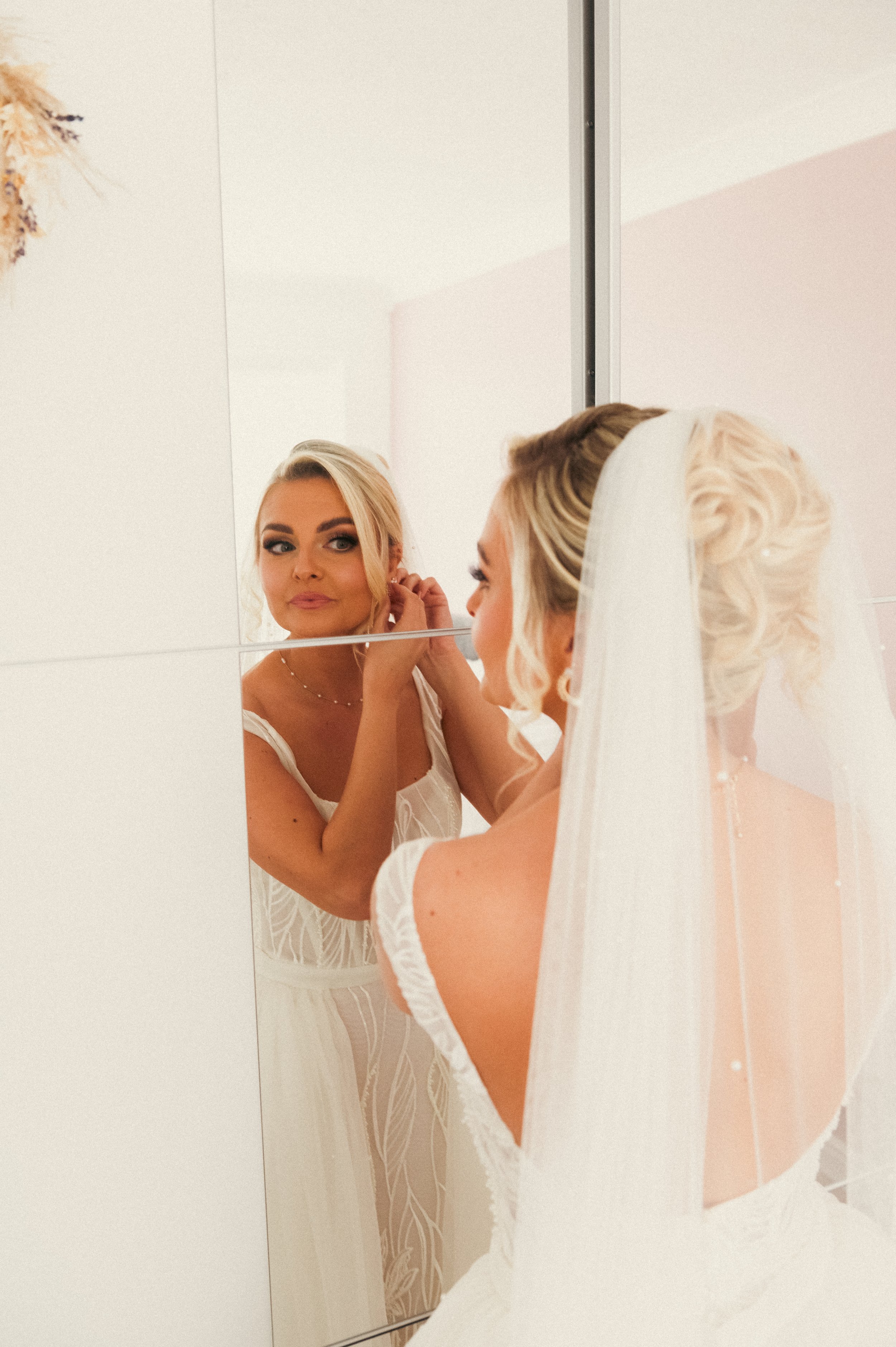Bride in a wedding dress putting on earrings while looking into a mirror.