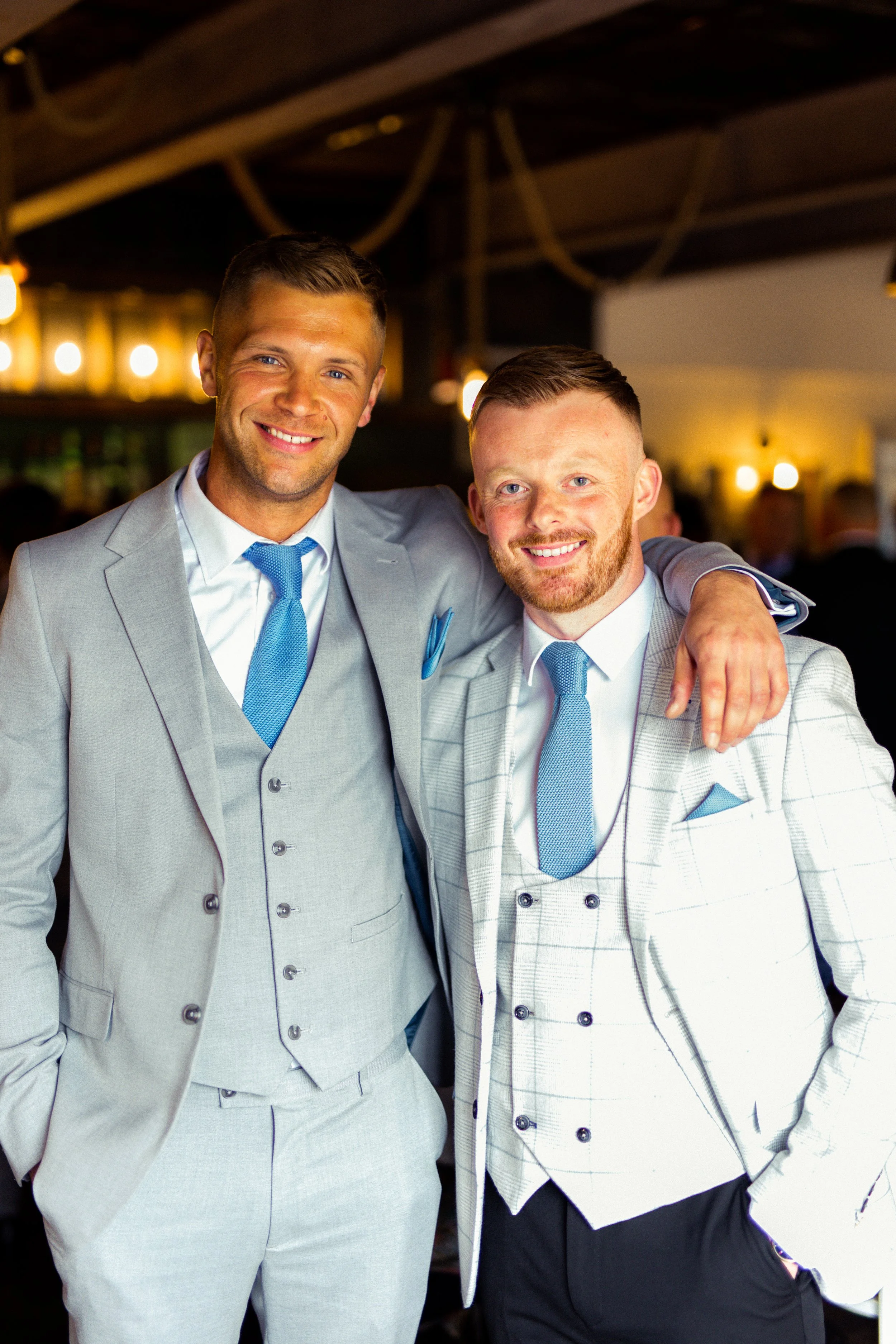 Two men in suits smiling at a social event, one with his arm around the other.