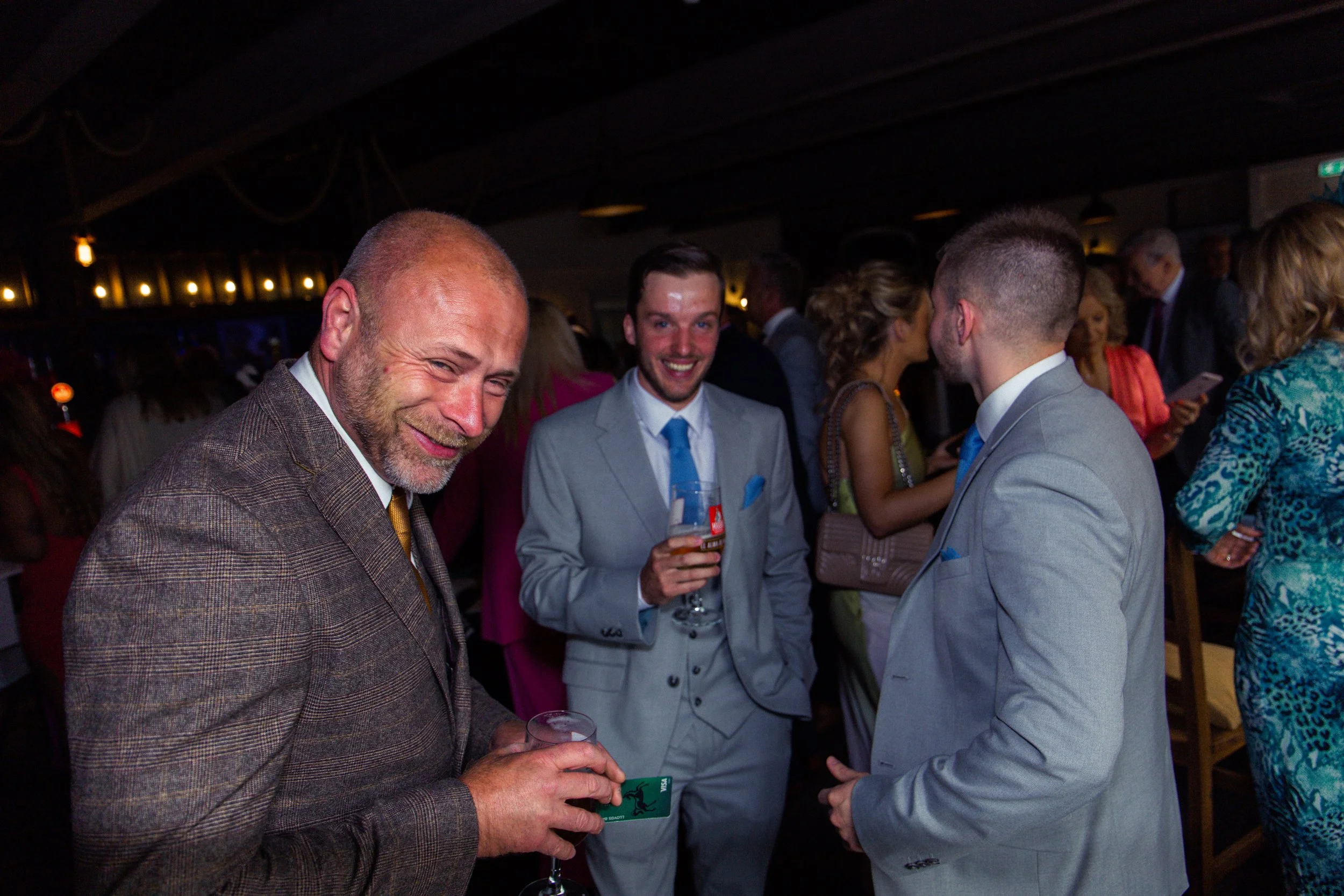 Group of people dressed in formal attire mingling at a social event or party, holding drinks and engaging in conversation.