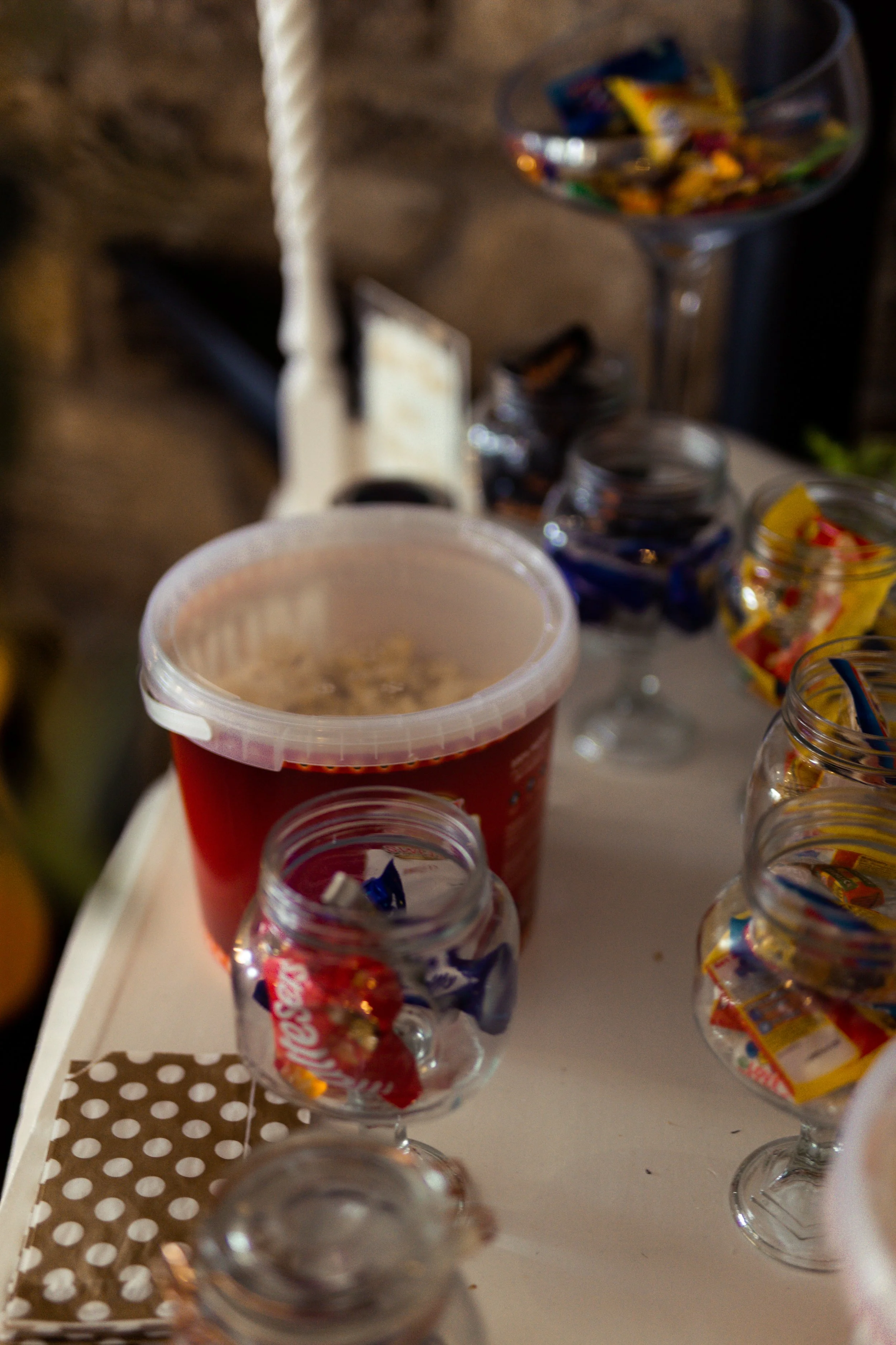 Assorted candies in glass jars and a container on a white table.
