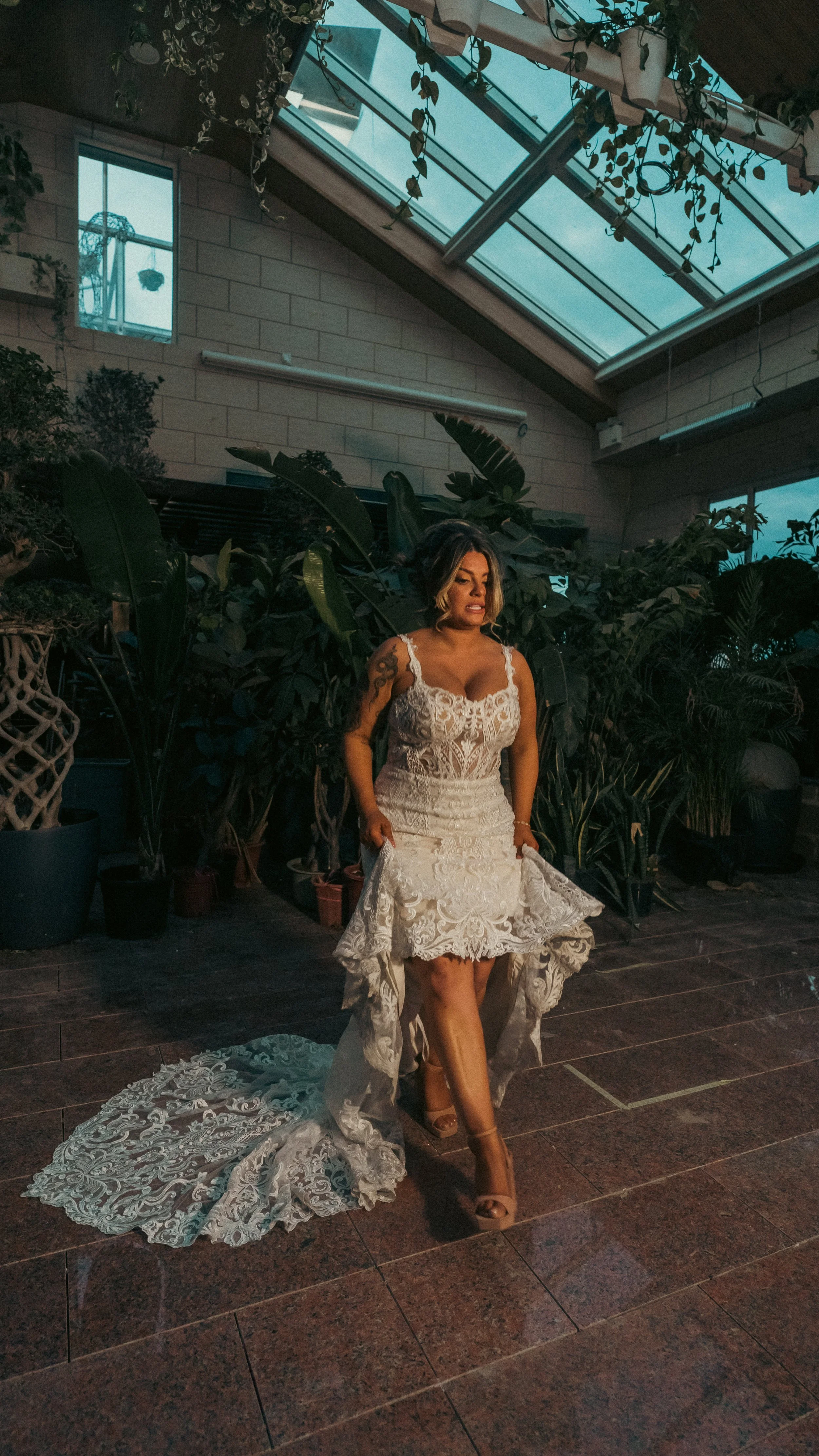 Woman in a white lace wedding dress inside a greenhouse with plants