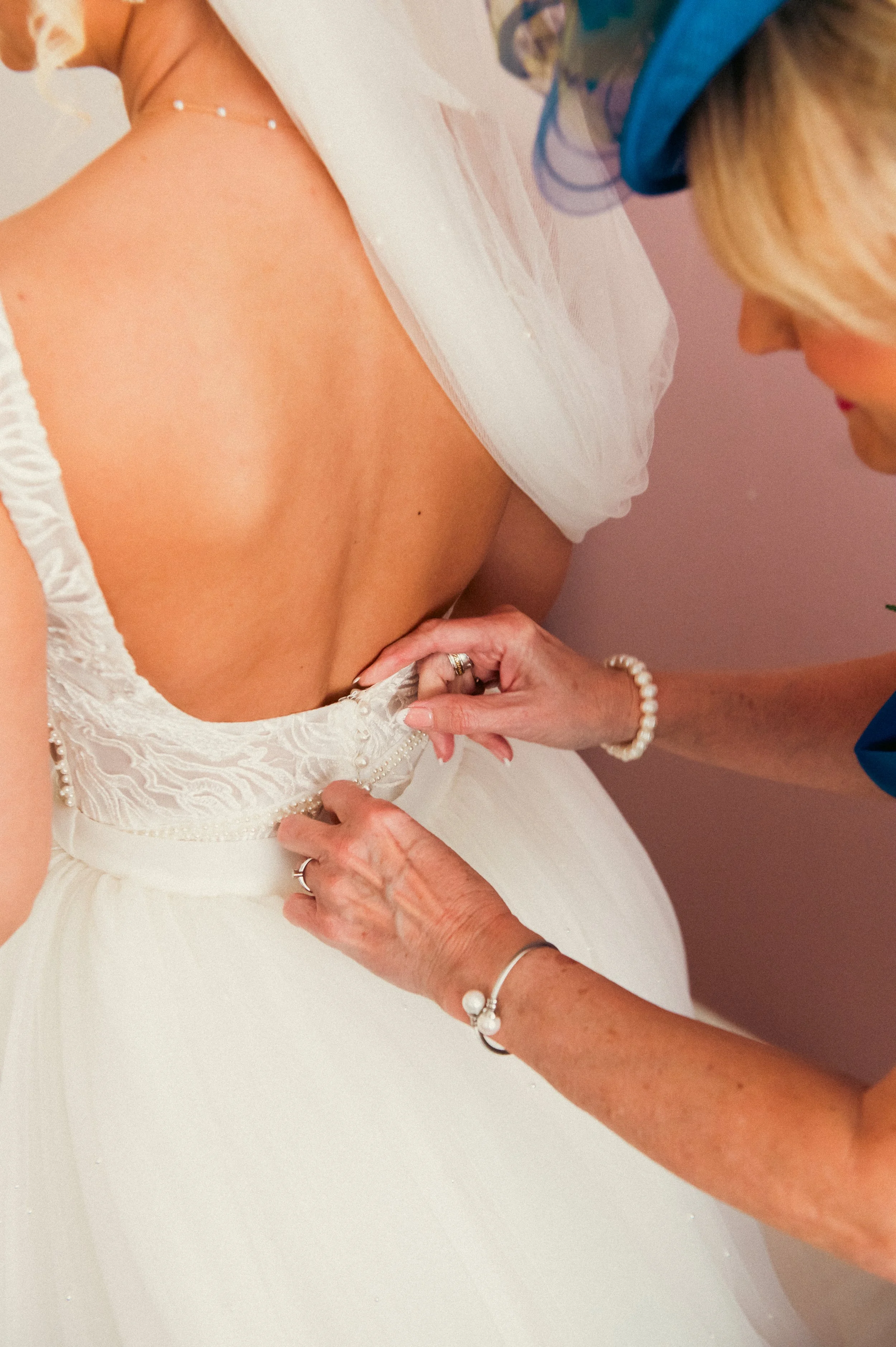 A woman helping bride with her wedding dress, focusing on fastening the back of the dress.