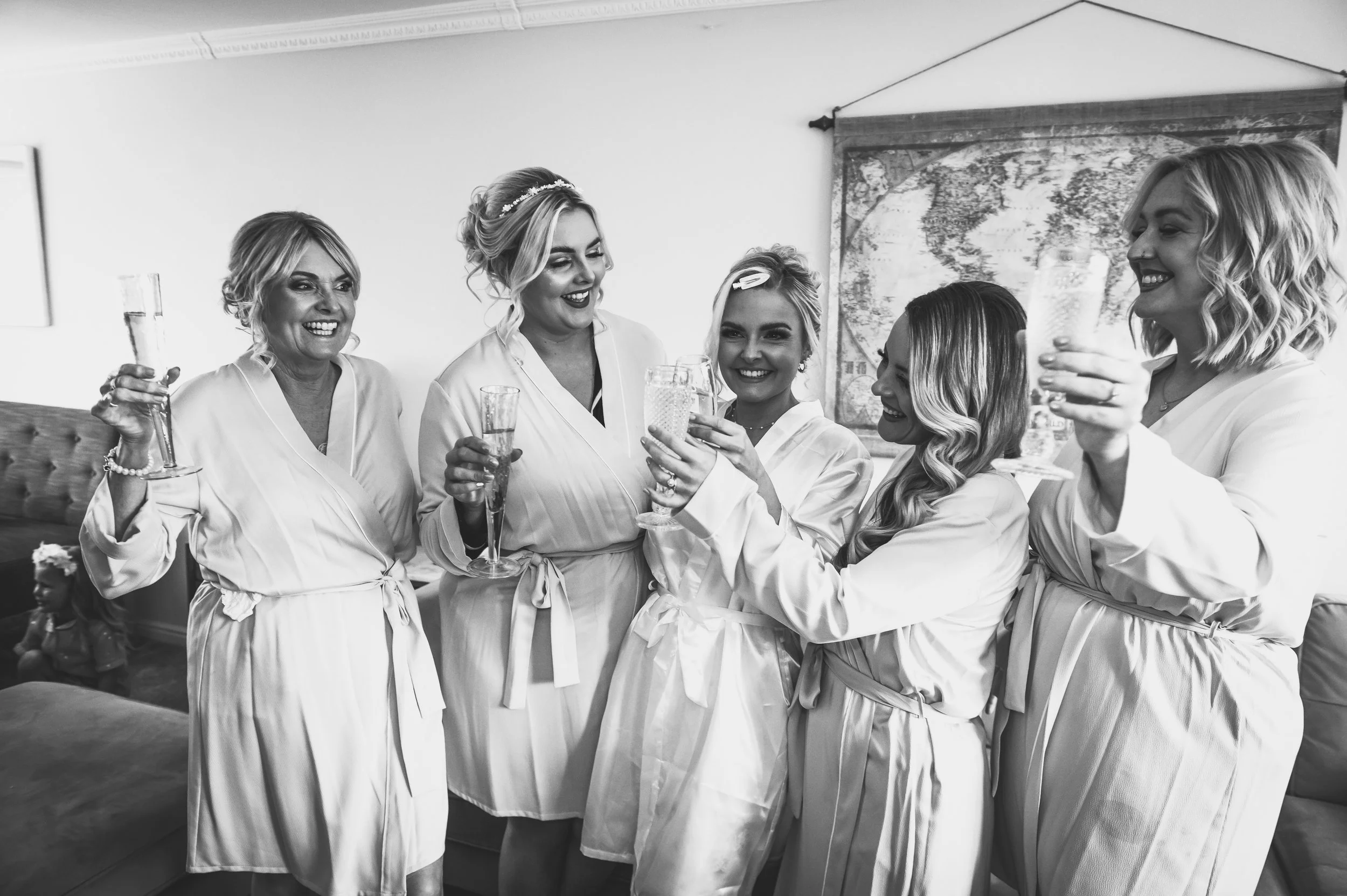 Six women in matching robes celebrating and raising glasses in a toast, smiling happily.