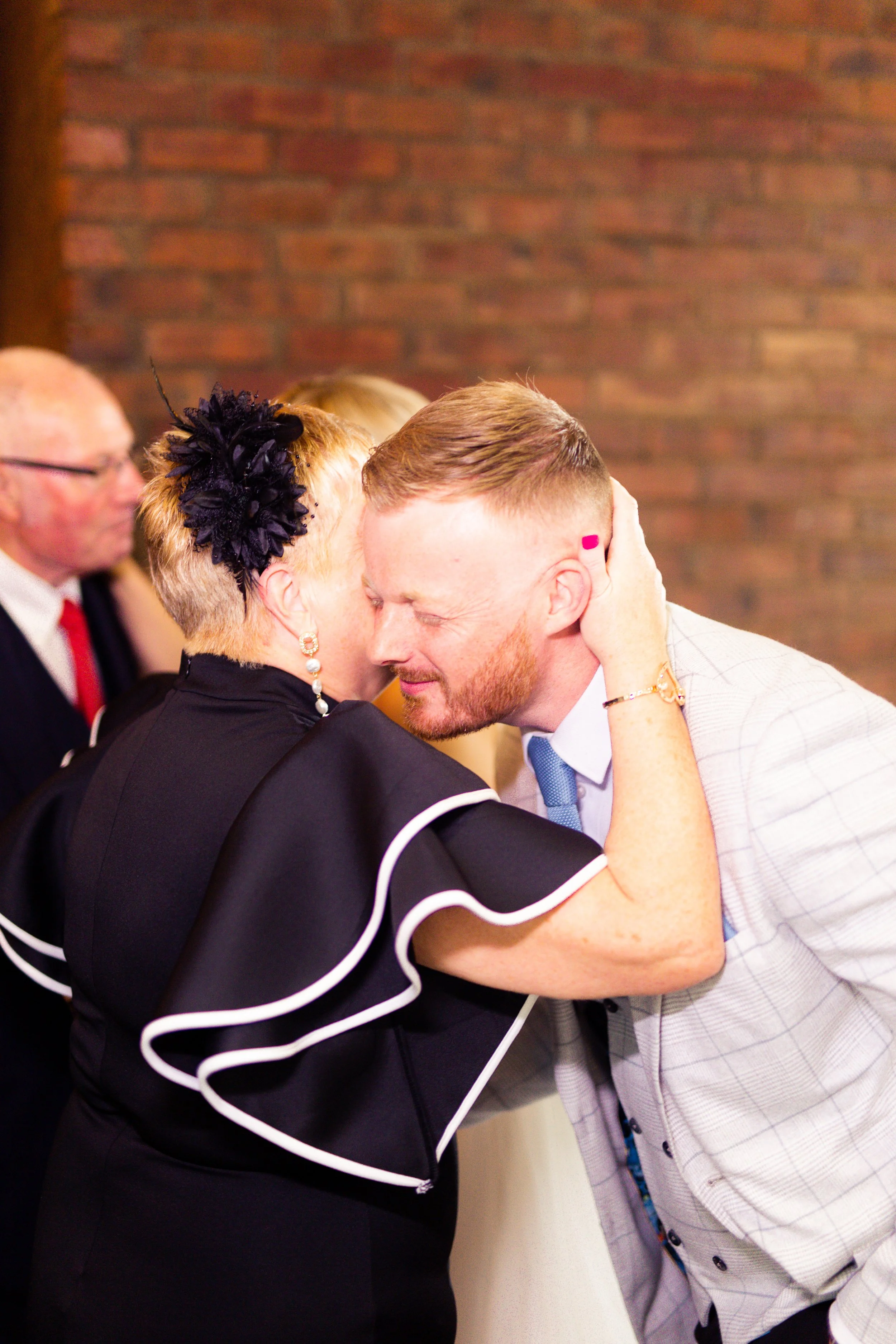 A woman embracing a man during a heartfelt moment at a social gathering, with a brick wall in the background.