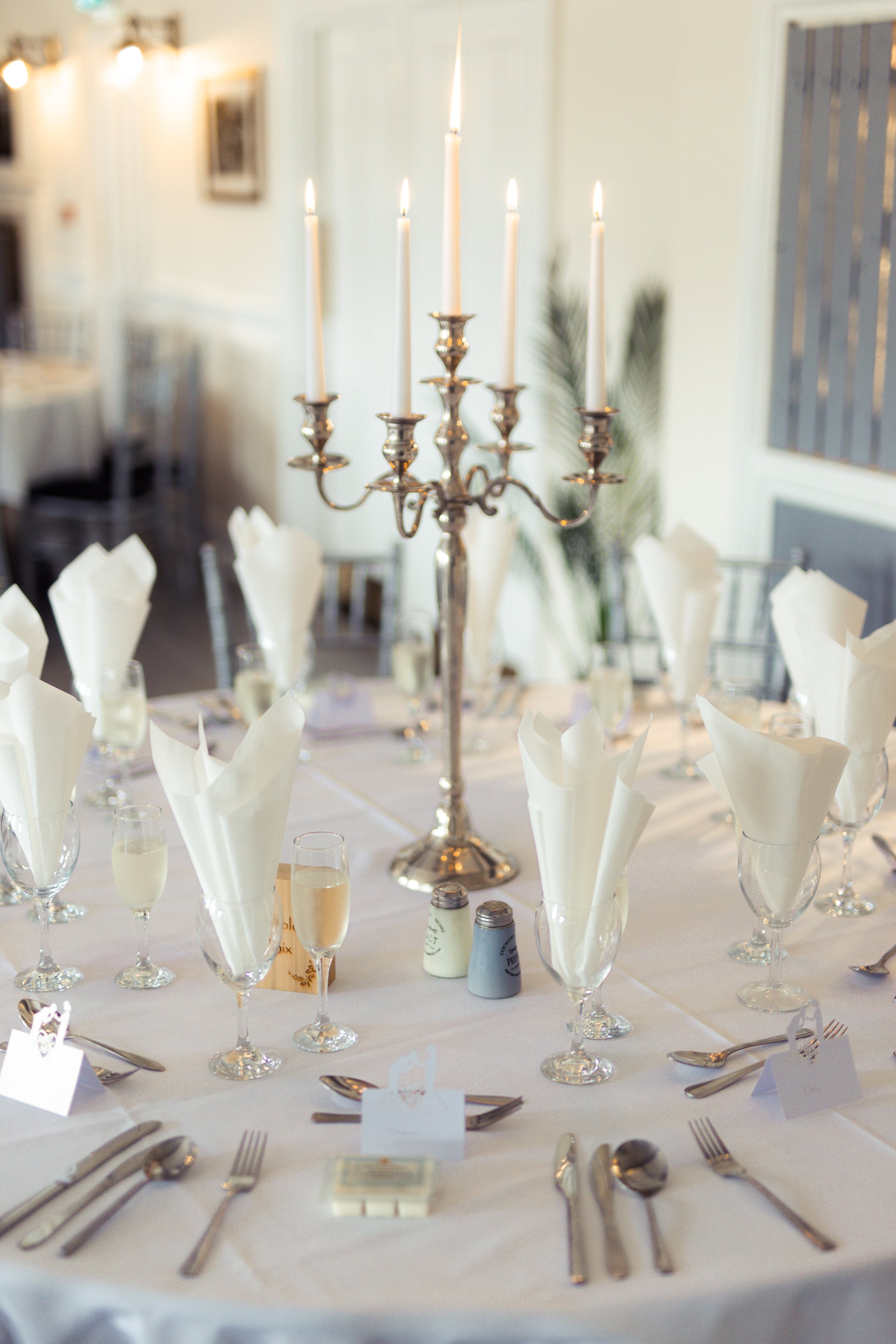 Table setting with white napkins, wine glasses, and a silver candelabrum with lit candles at an elegant event.