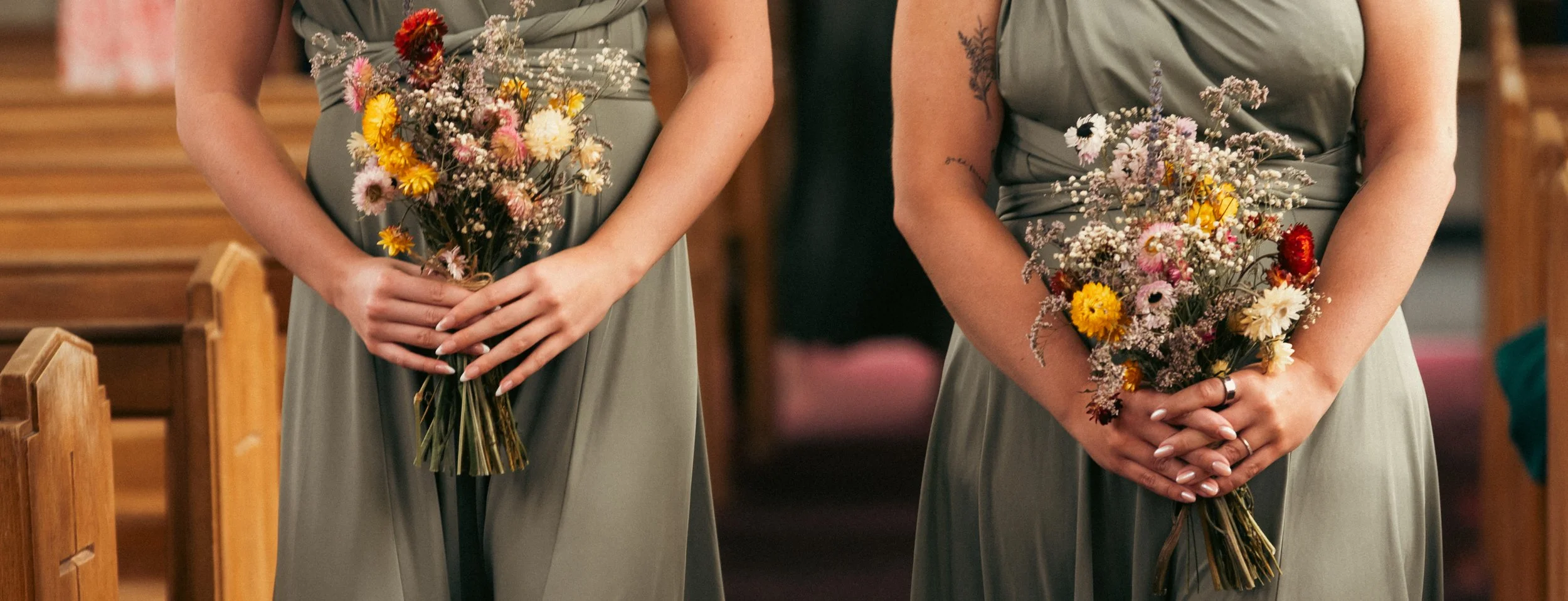 Close-up of two women in gray dresses holding bouquets of mixed flowers during a wedding or ceremony.