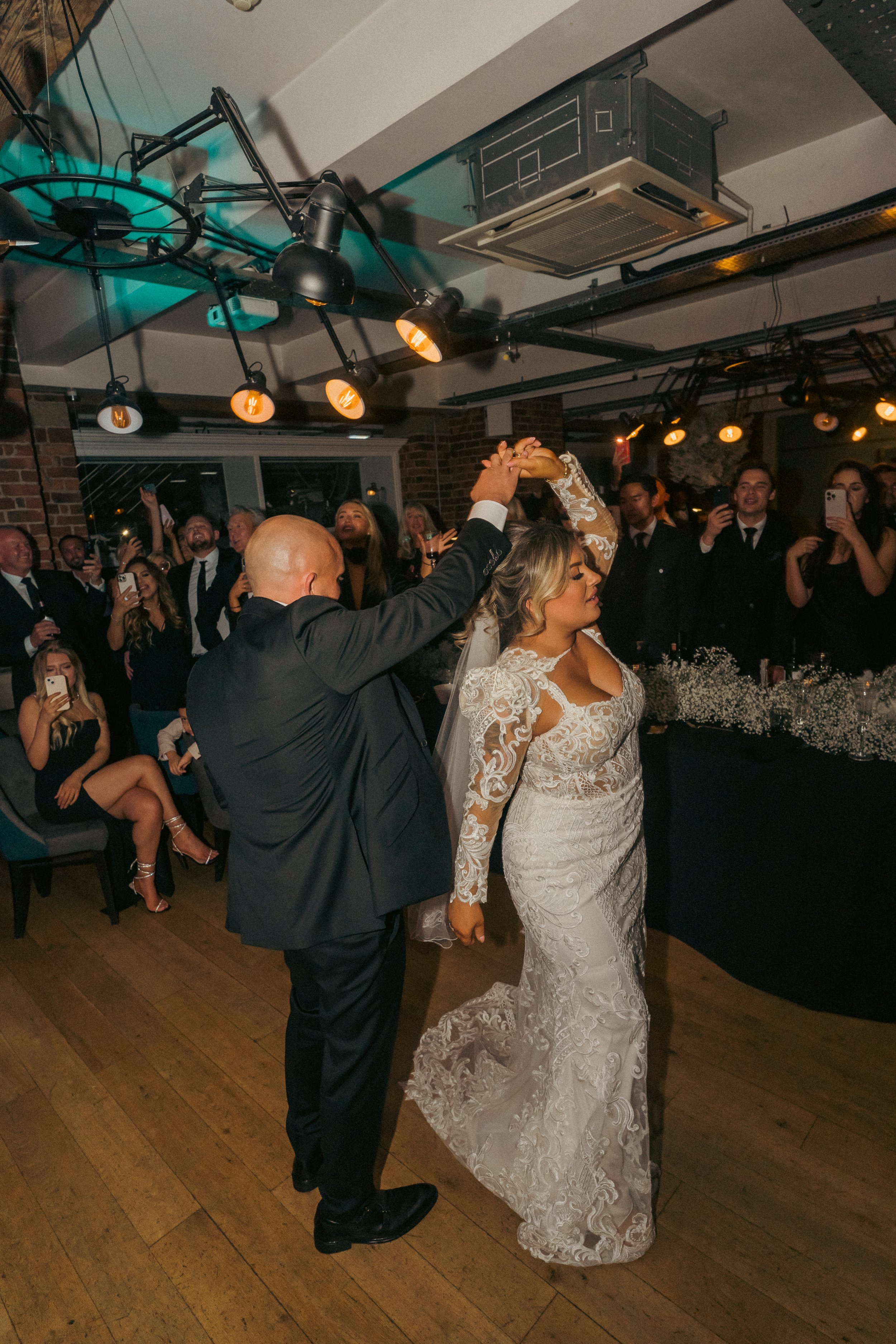 Bride and groom dancing at their wedding reception with guests watching and taking photos.