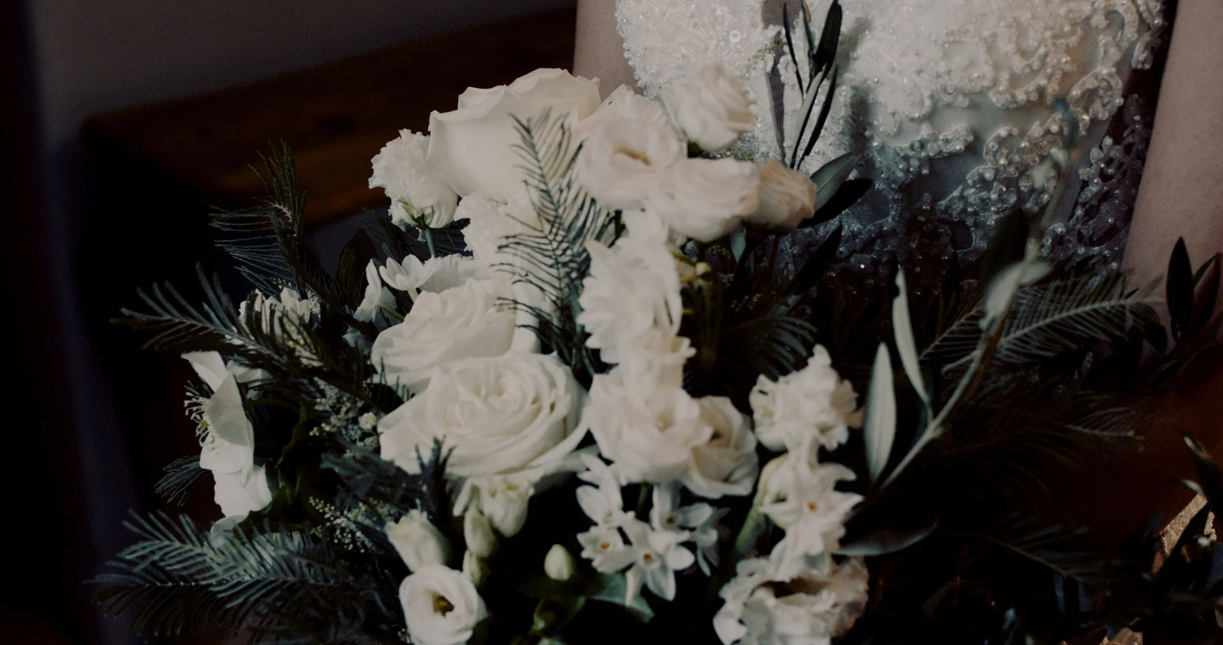 White floral bouquet with roses, baby’s breath, and dark green foliage, with a sparkling textured background.