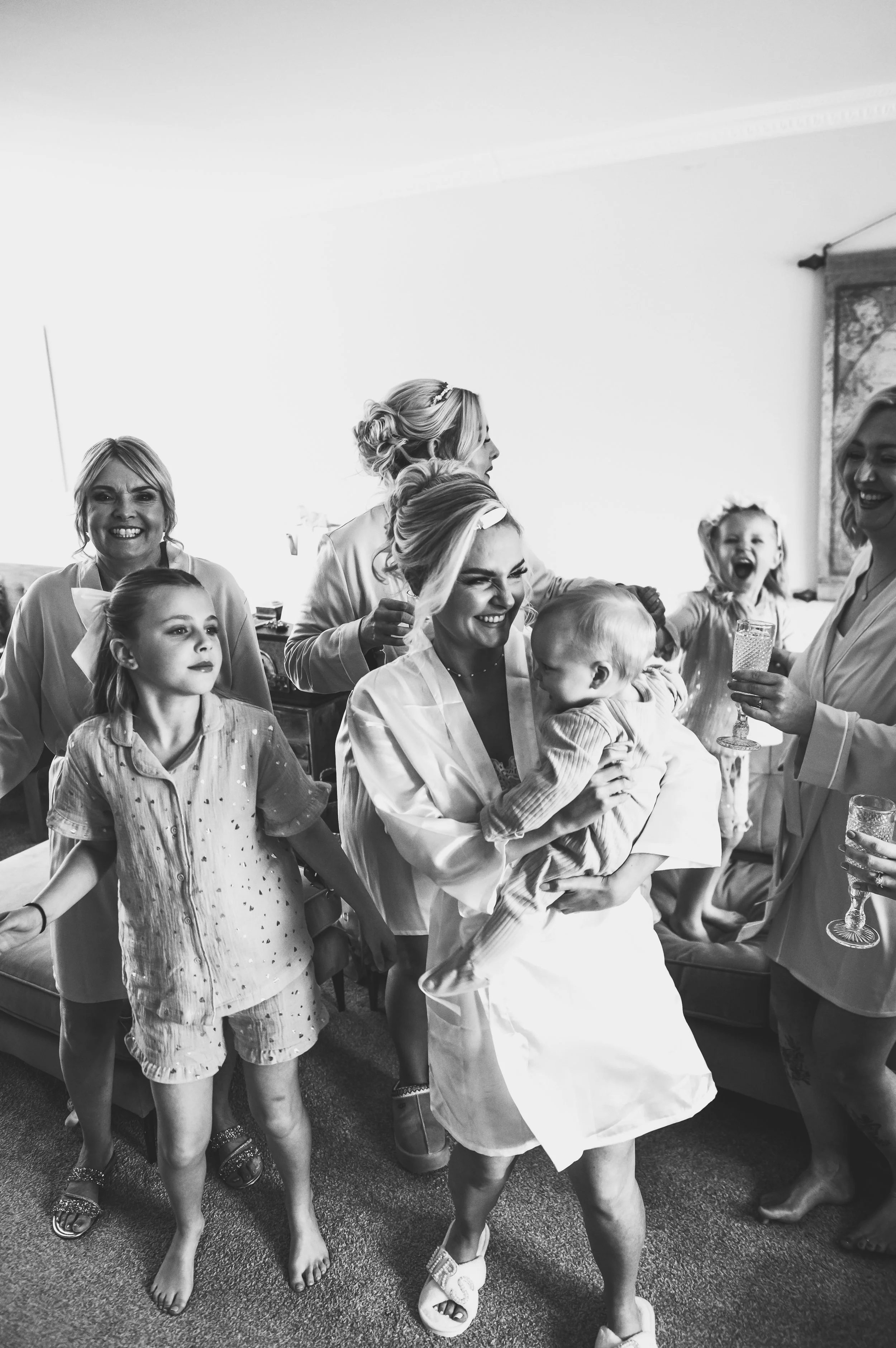A group of women and children celebrating indoors, with one woman holding a toddler and others smiling and holding glasses.