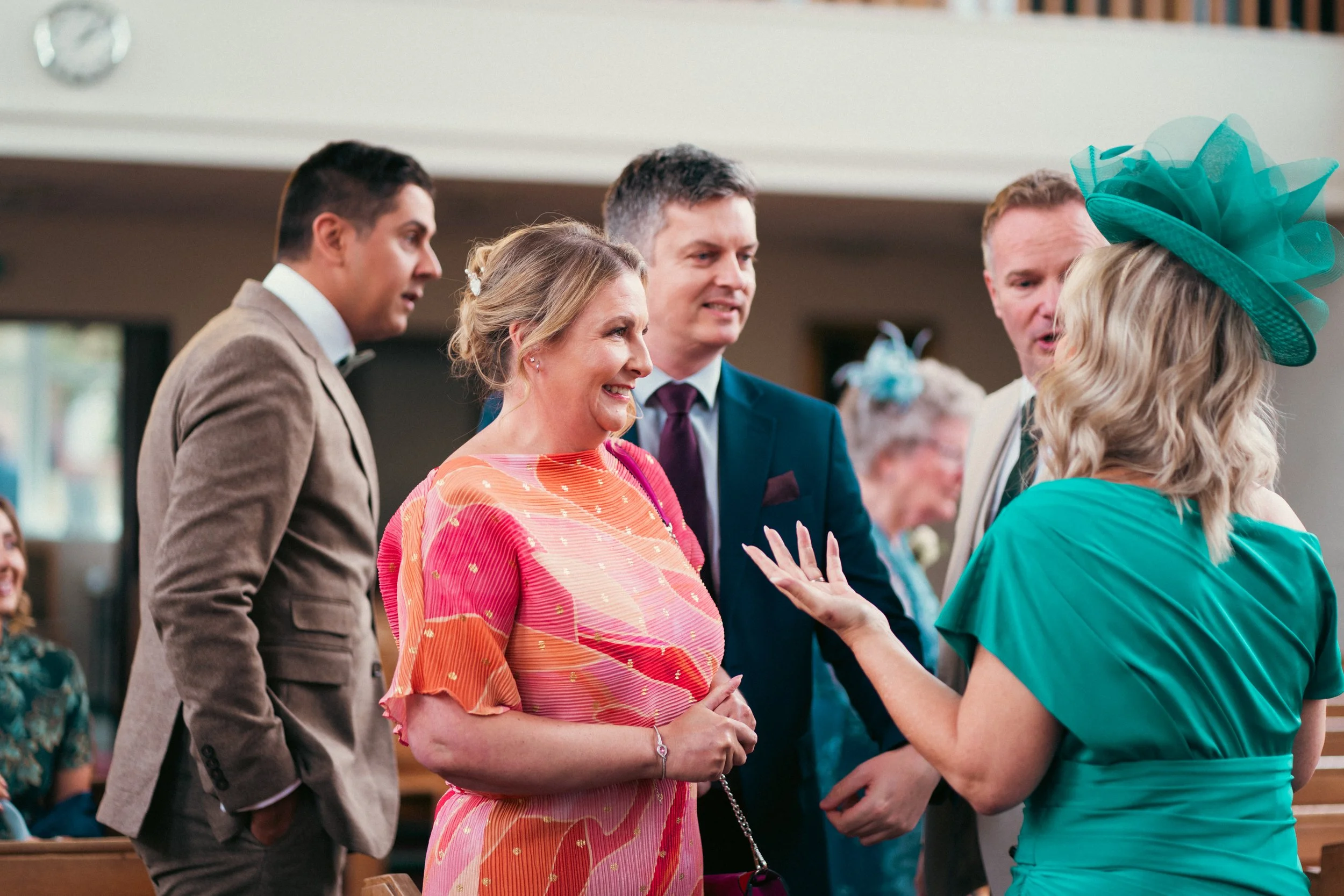 People at a wedding reception talking and smiling, with women in colorful dresses and men in suits.