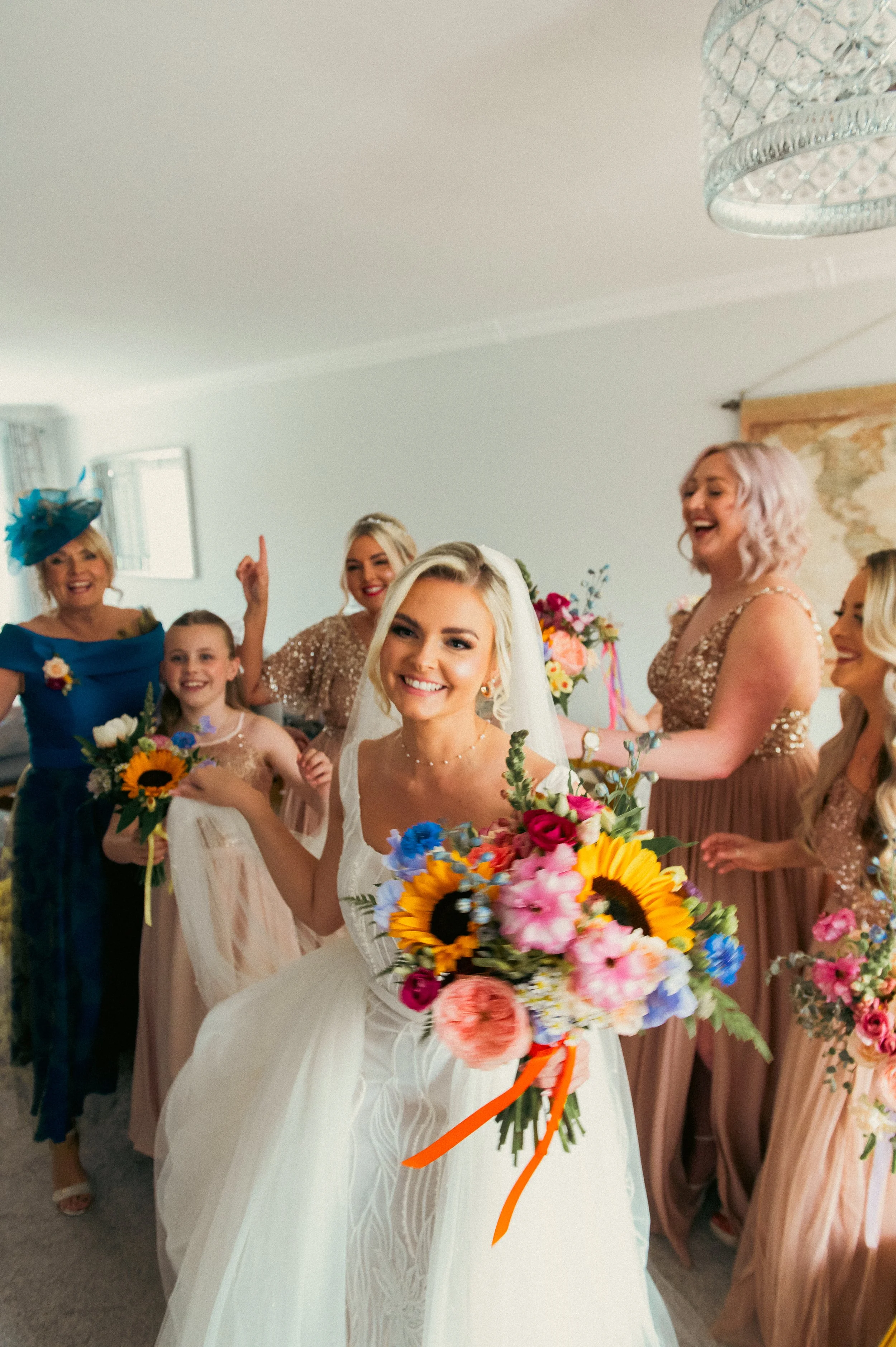 Bride with a bouquet of colorful flowers surrounded by bridesmaids and family in celebration.