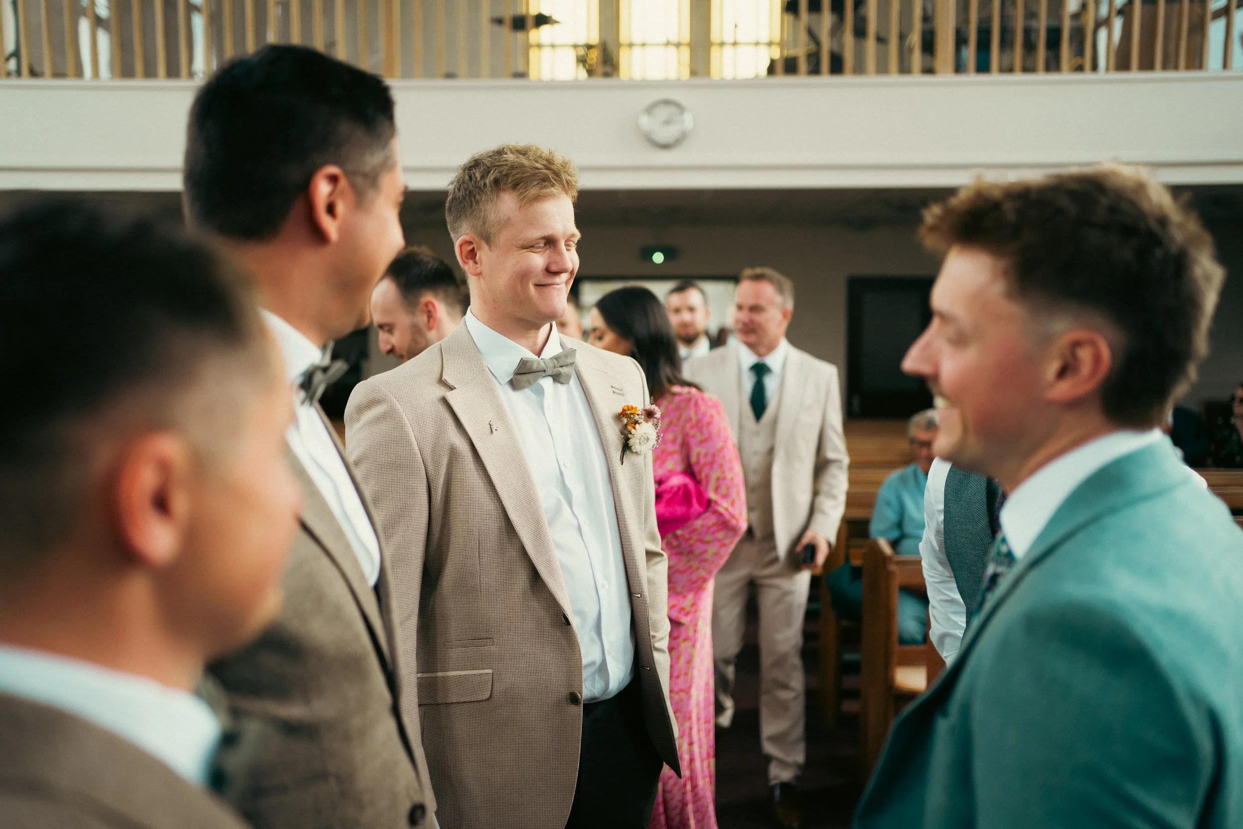Absolutely thrilled groom and groomsmen smiling at each other during a wedding ceremony in a church.