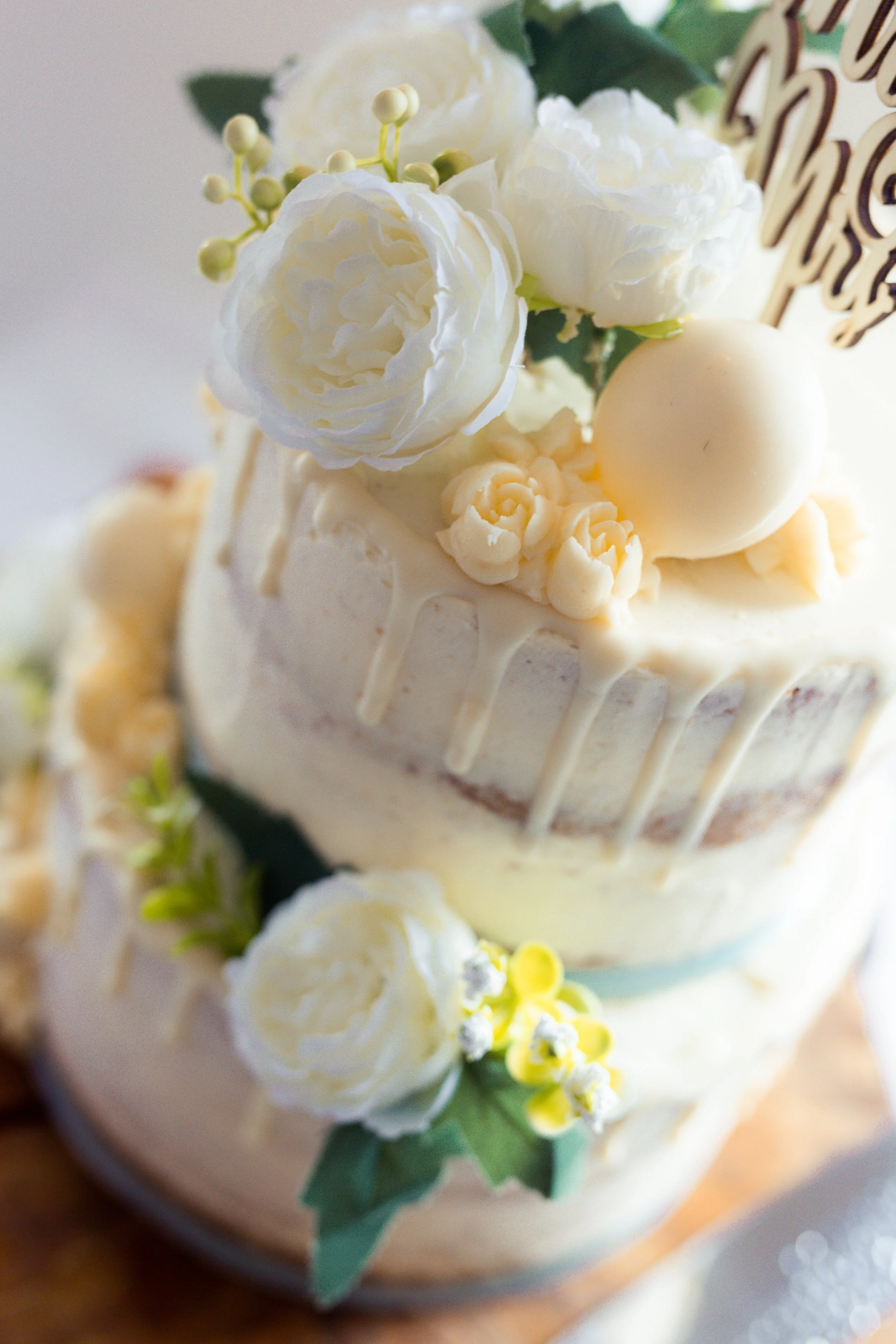 A two-tiered white wedding cake decorated with white roses, floral accents, and a cake topper.