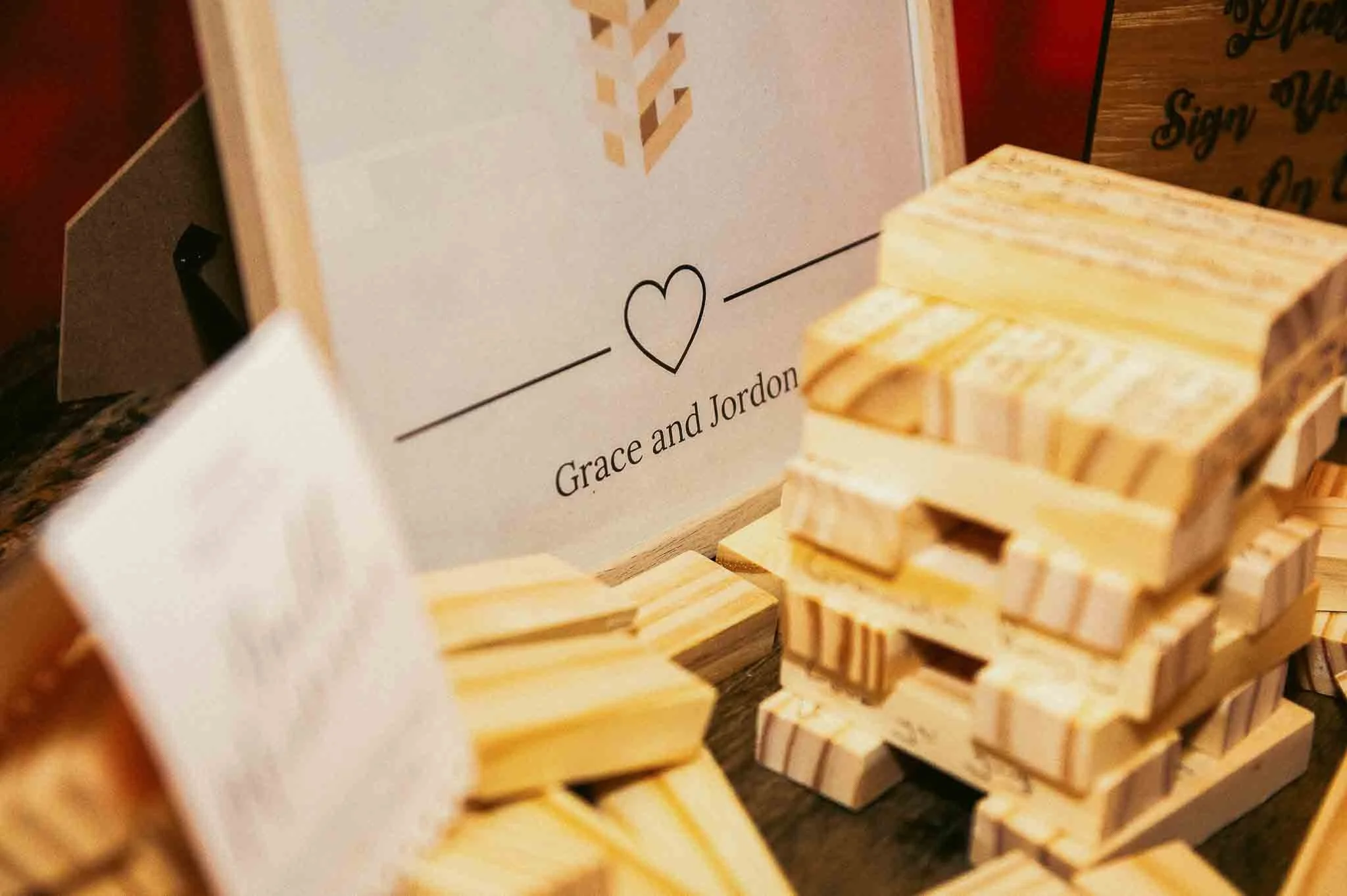 Stacked wooden Jenga blocks near a sign with a heart and the names 'Grace and Jordon' written on it.
