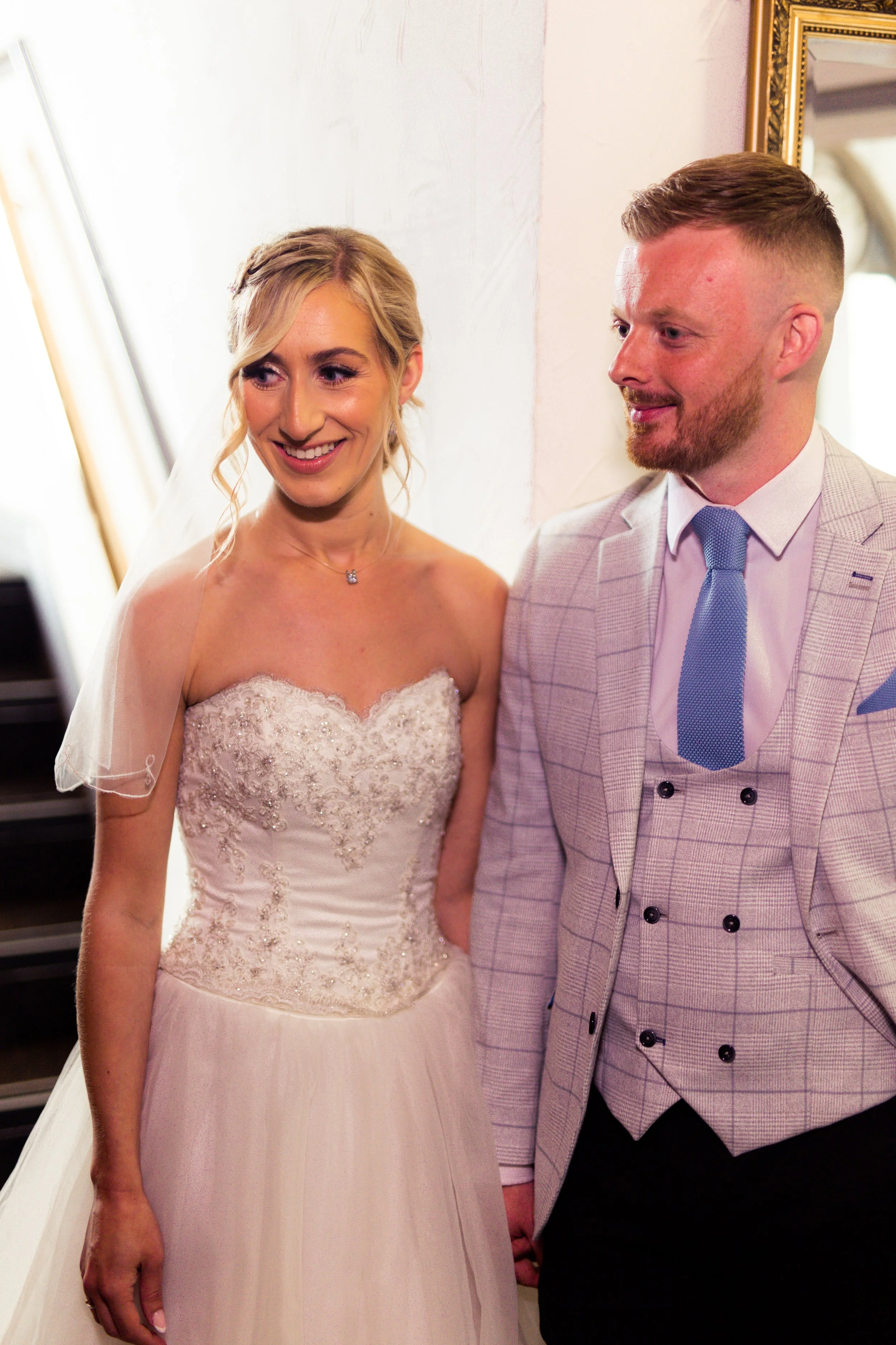A bride and groom standing together, smiling during their wedding ceremony, inside a decorated venue.