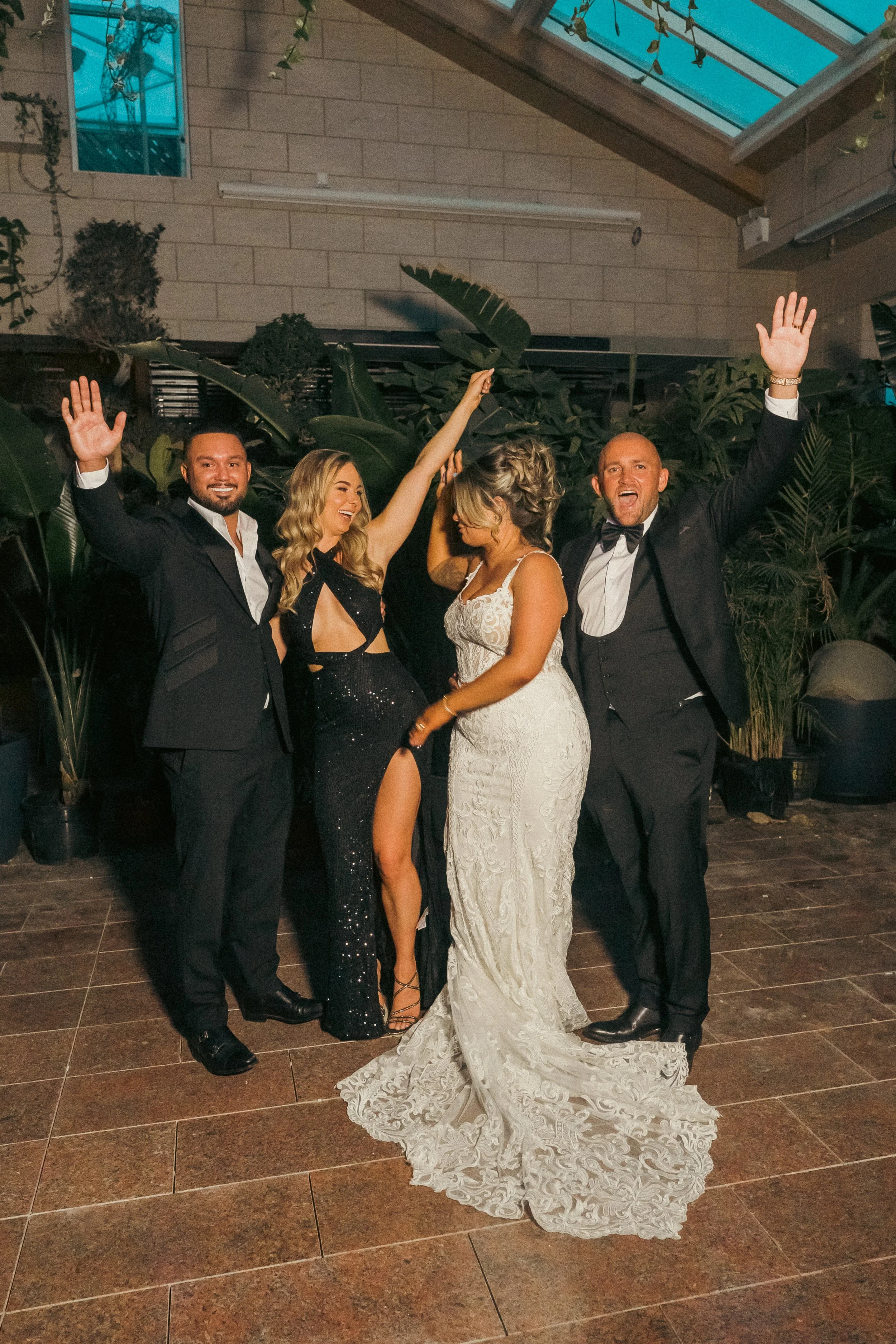 Group of four people at a celebration, two men in suits and two women in formal dresses, dancing and celebrating.