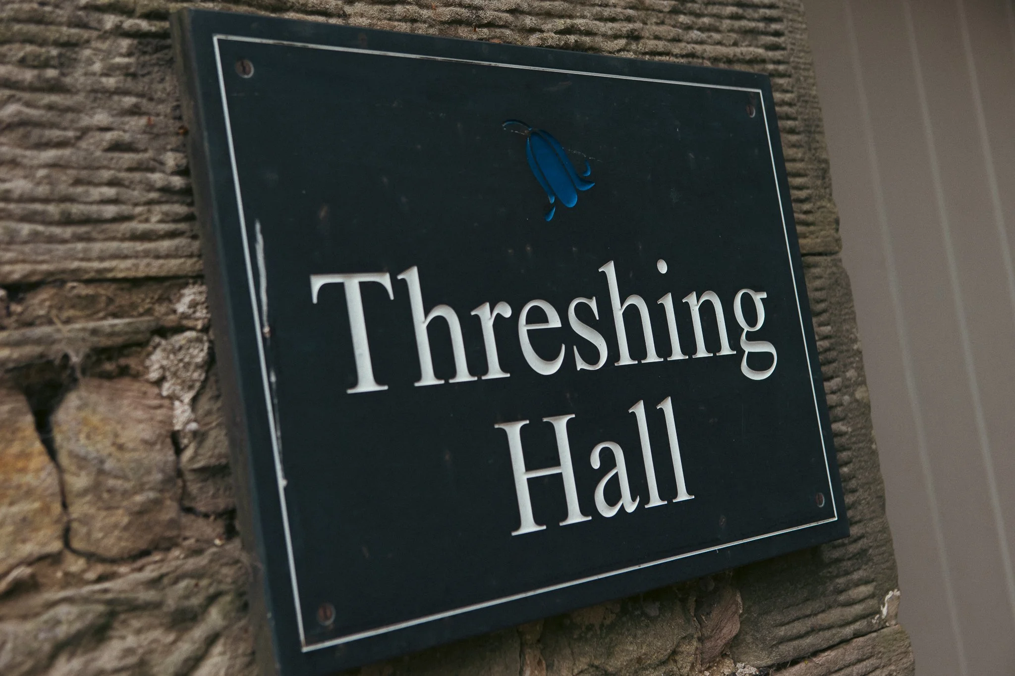 A black sign with white text reading 'Threshing Hall' mounted on a stone wall.