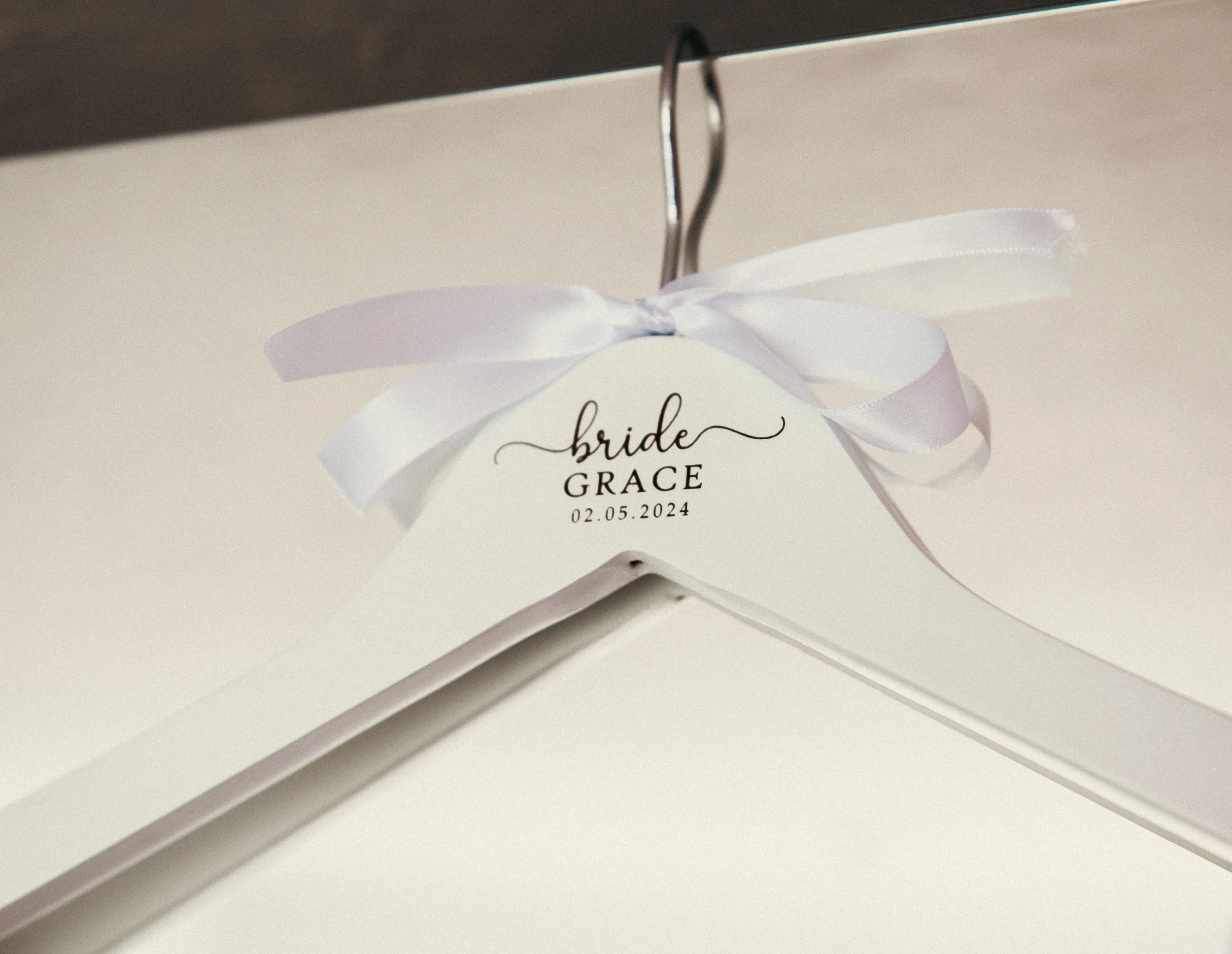 White hanger with a star-shaped tag that reads 'bride' and 'GRACE' with the date 02.05.2024, decorated with a white satin ribbon.