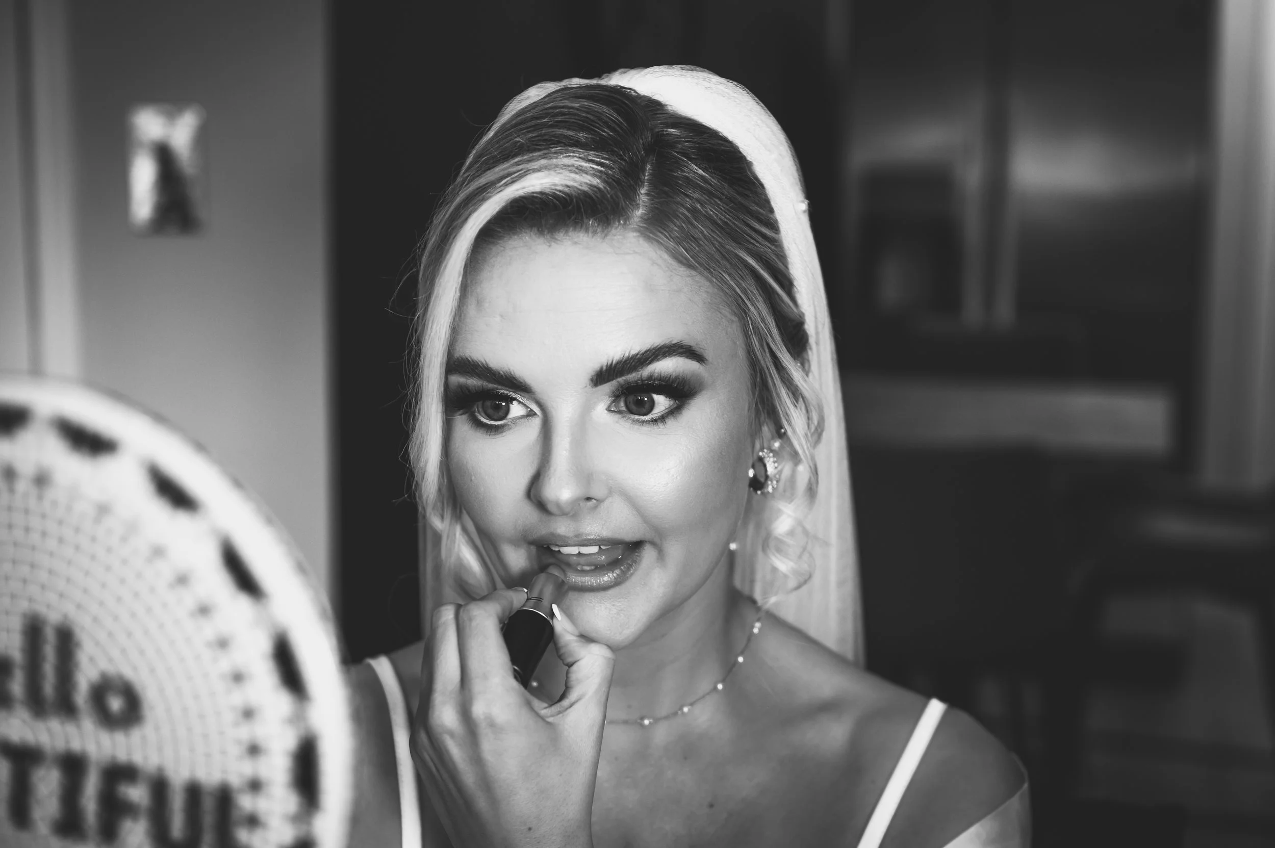 A woman with blonde hair and makeup applying lipstick in front of a mirror.