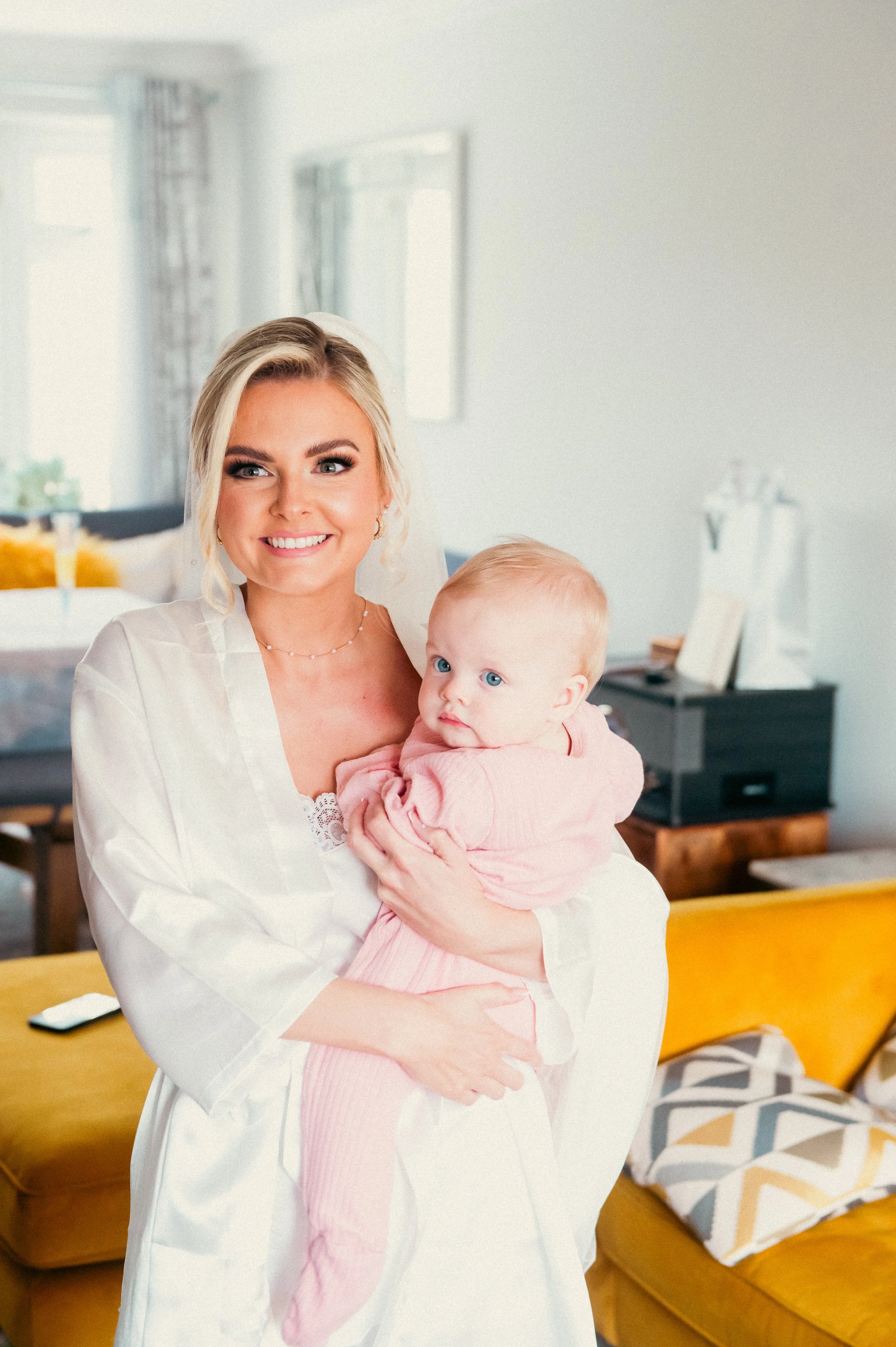 A woman smiling and holding a baby girl in a brightly lit living room.