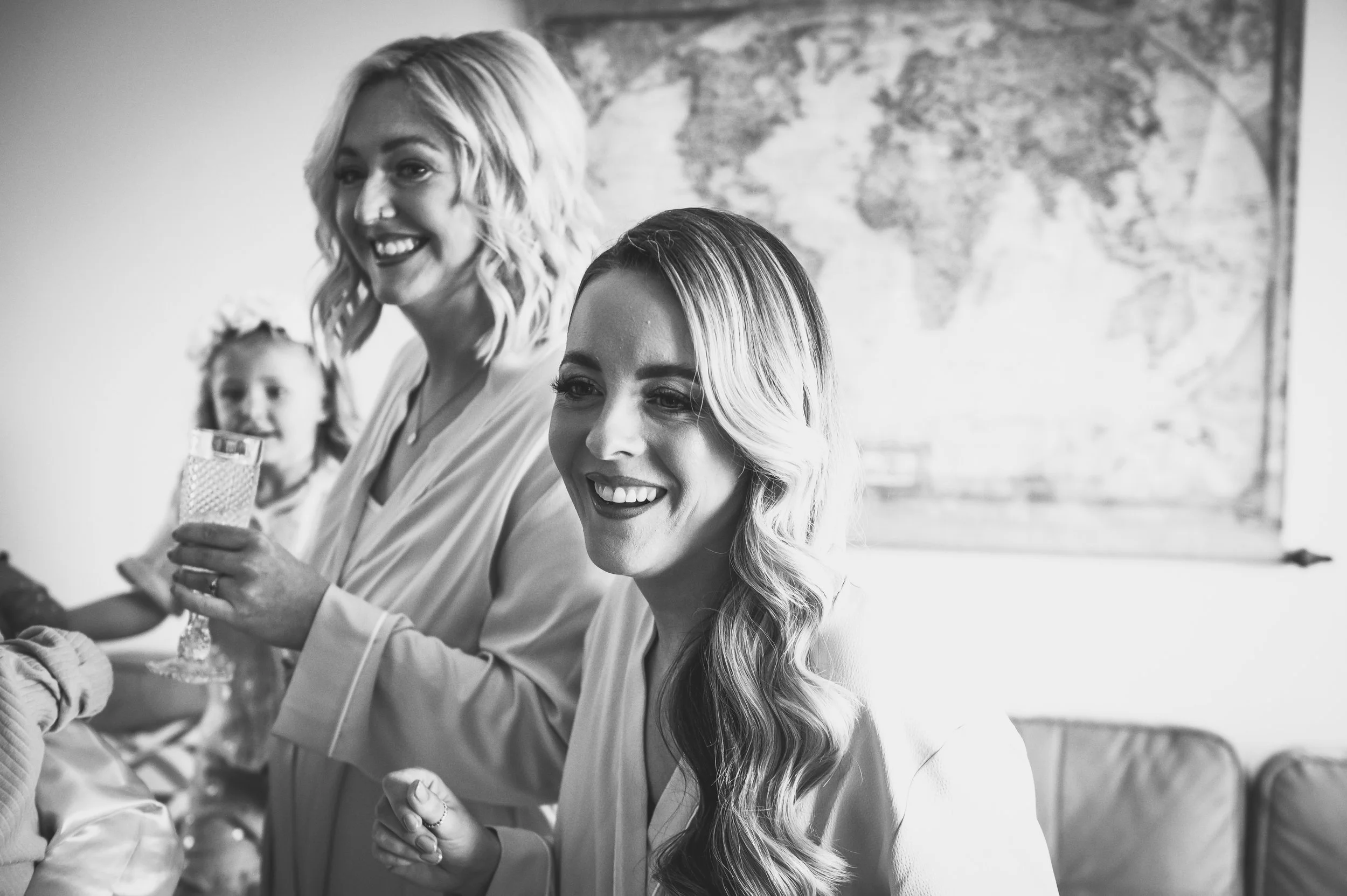 Black-and-white photo of three women smiling and holding glasses, with a world map on the wall behind them.