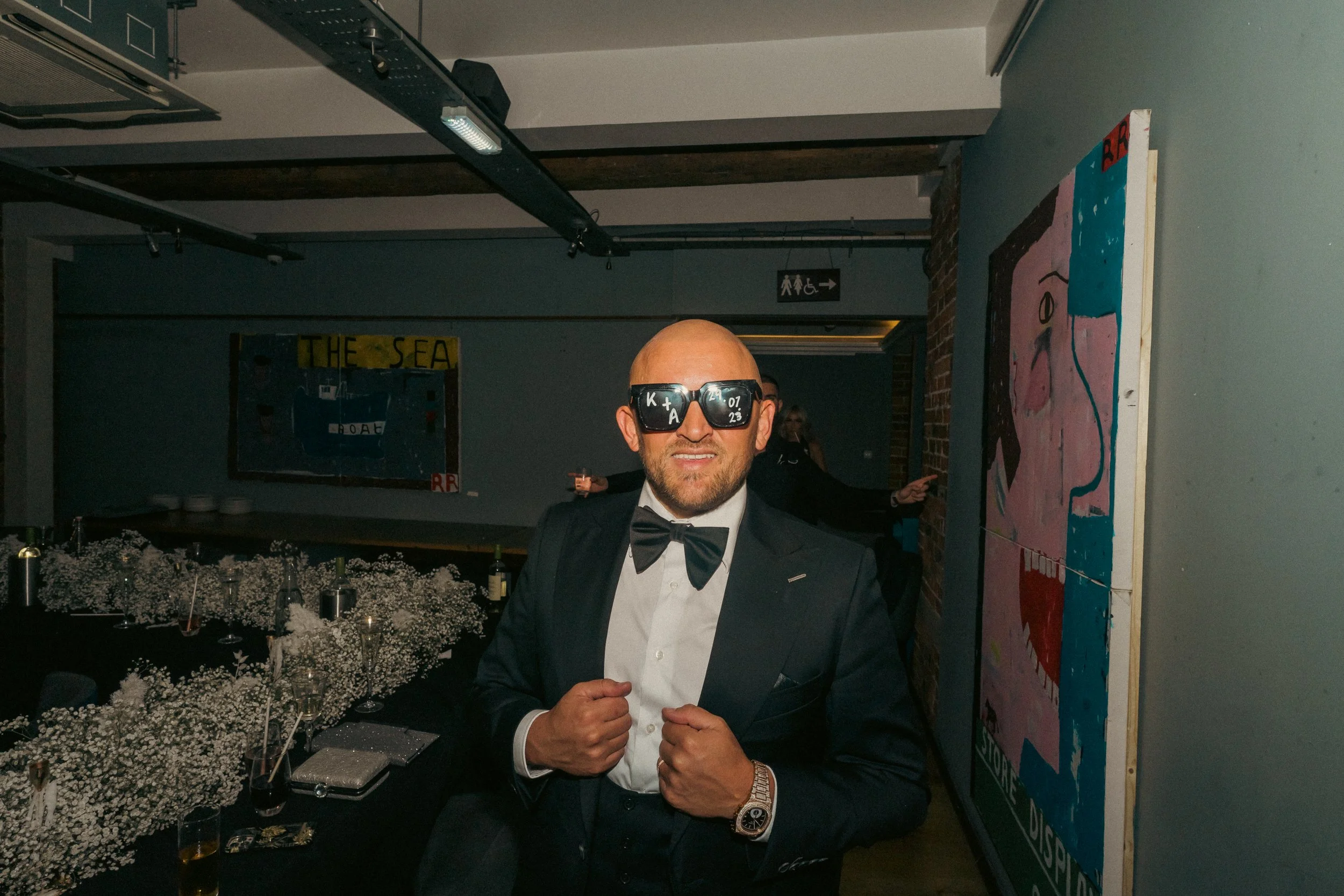 A man in a tuxedo with a bow tie and sunglasses posing at a formal event.
