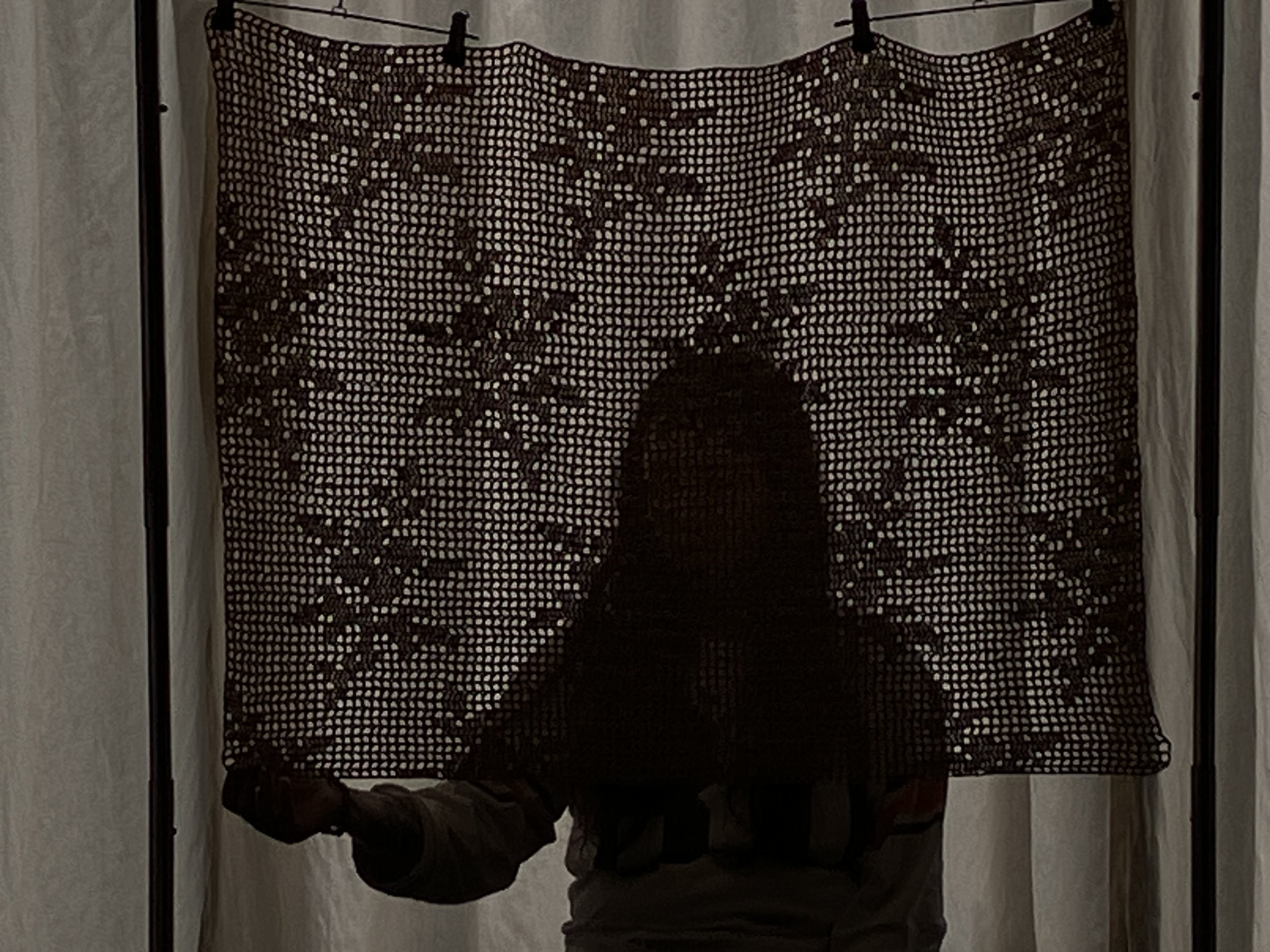 A person is hanging a black lace curtain with floral patterns on a railing between two curtains.