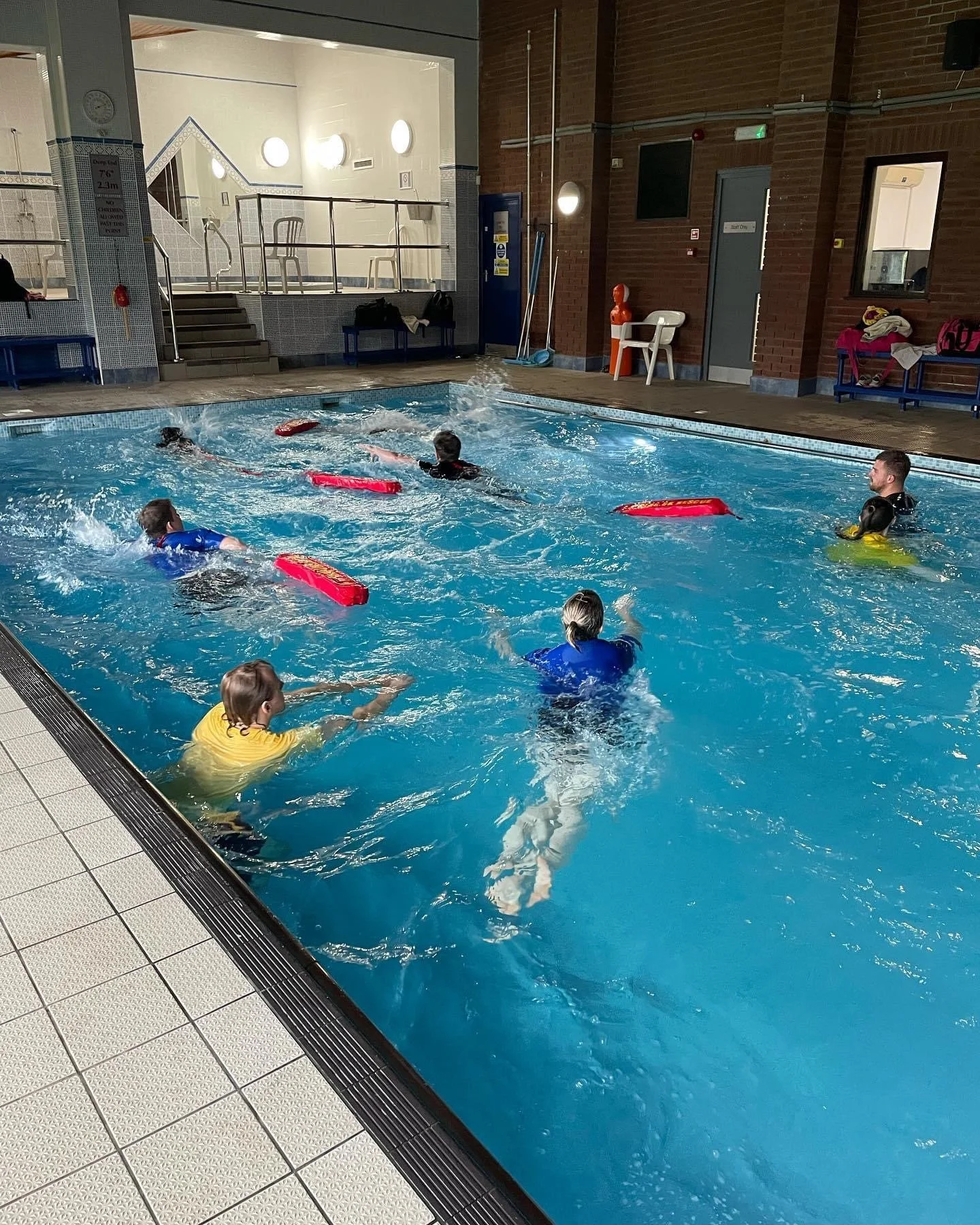 Children and an adult in a swimming pool participating in a swimming lesson or activity.