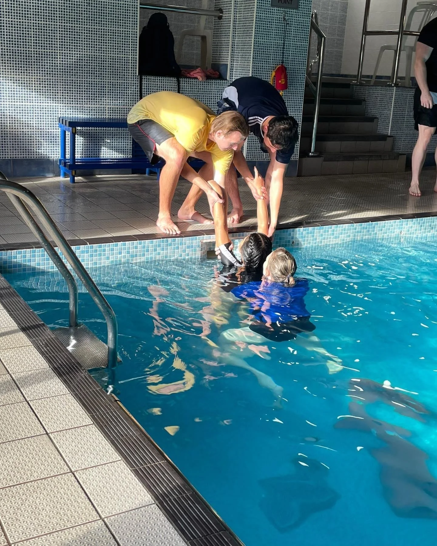 Swimmers being rescued from the pool by two men on the side of the pool.