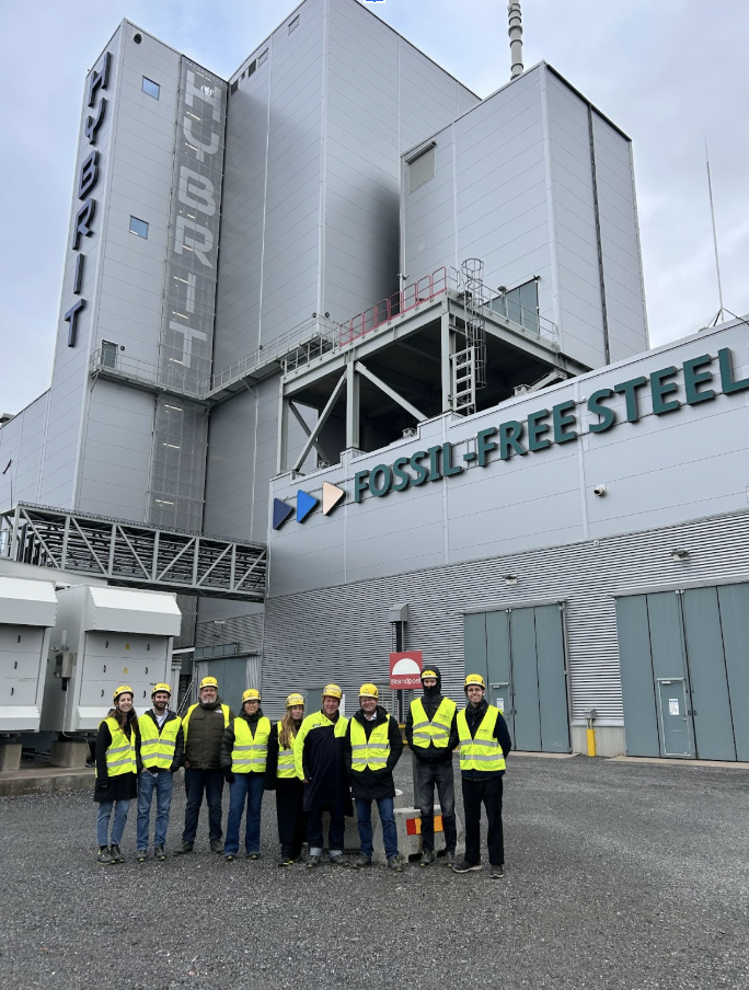A group of people wearing yellow safety vests pose for a photo in front of an industrial facility in Luleå, Sweden.