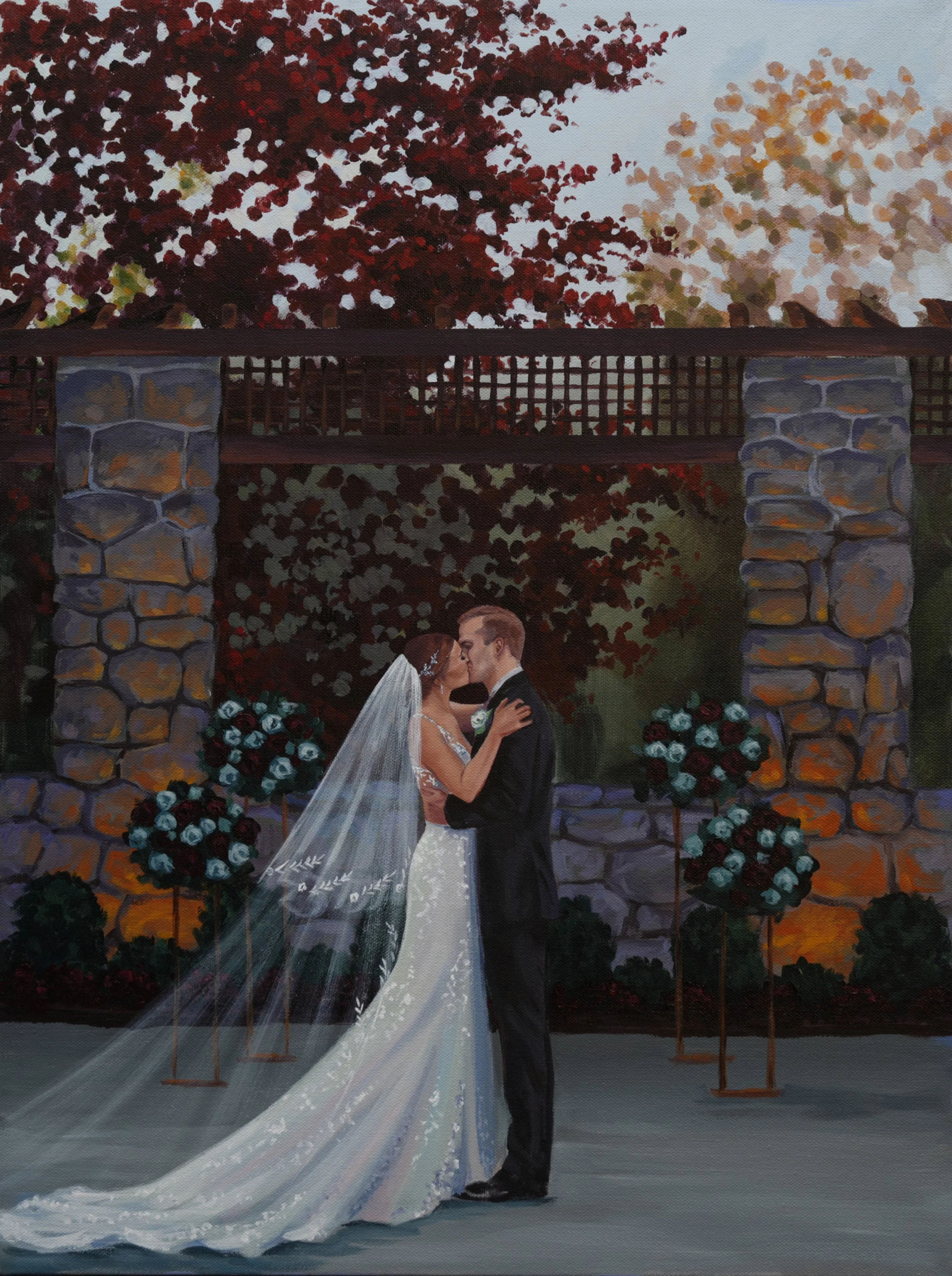 A bride and groom kissing during their wedding ceremony outdoors, with a stone and wood archway and floral arrangements in the background.