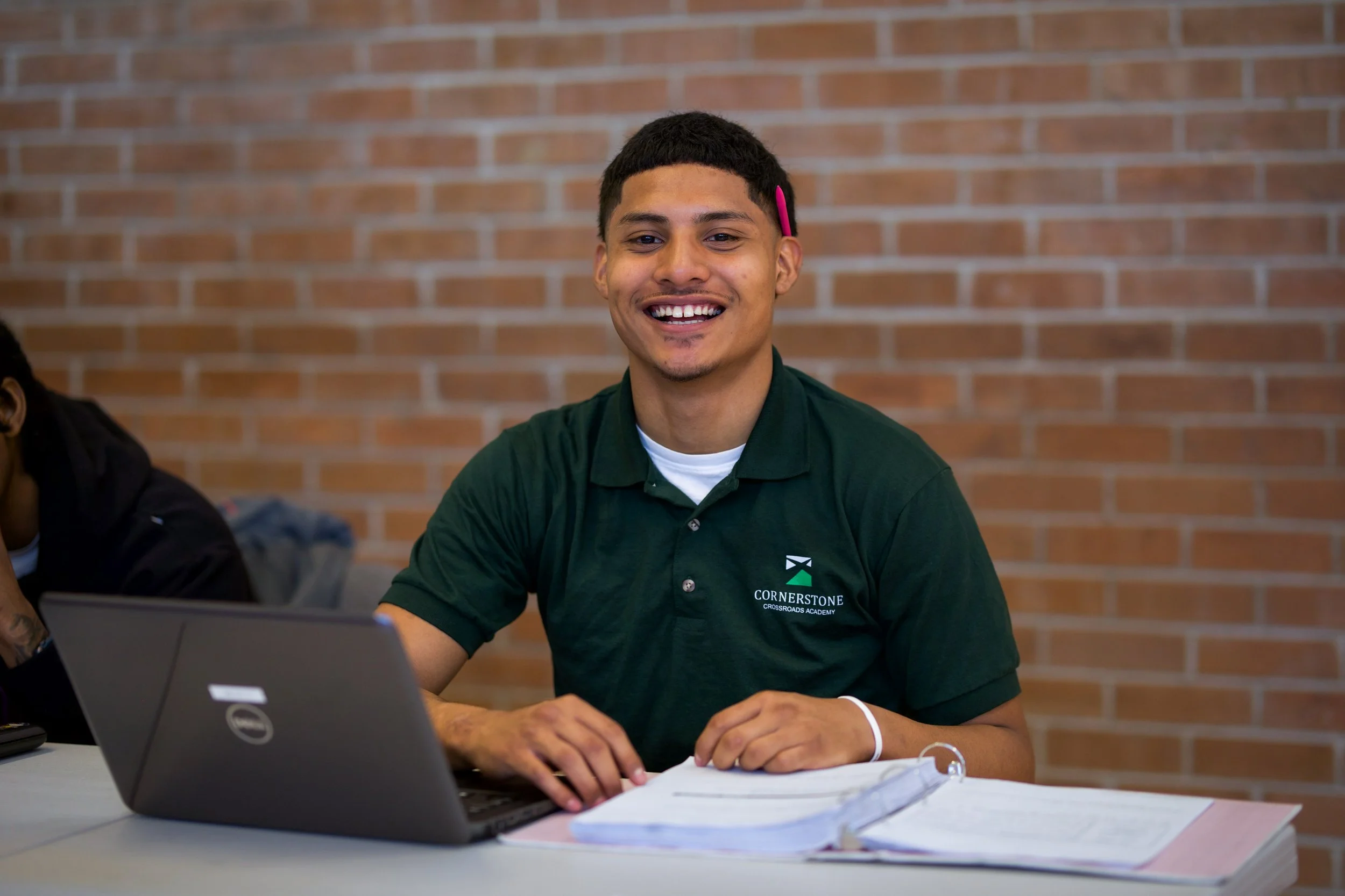 Male student smiling and sitting with computer and notebook