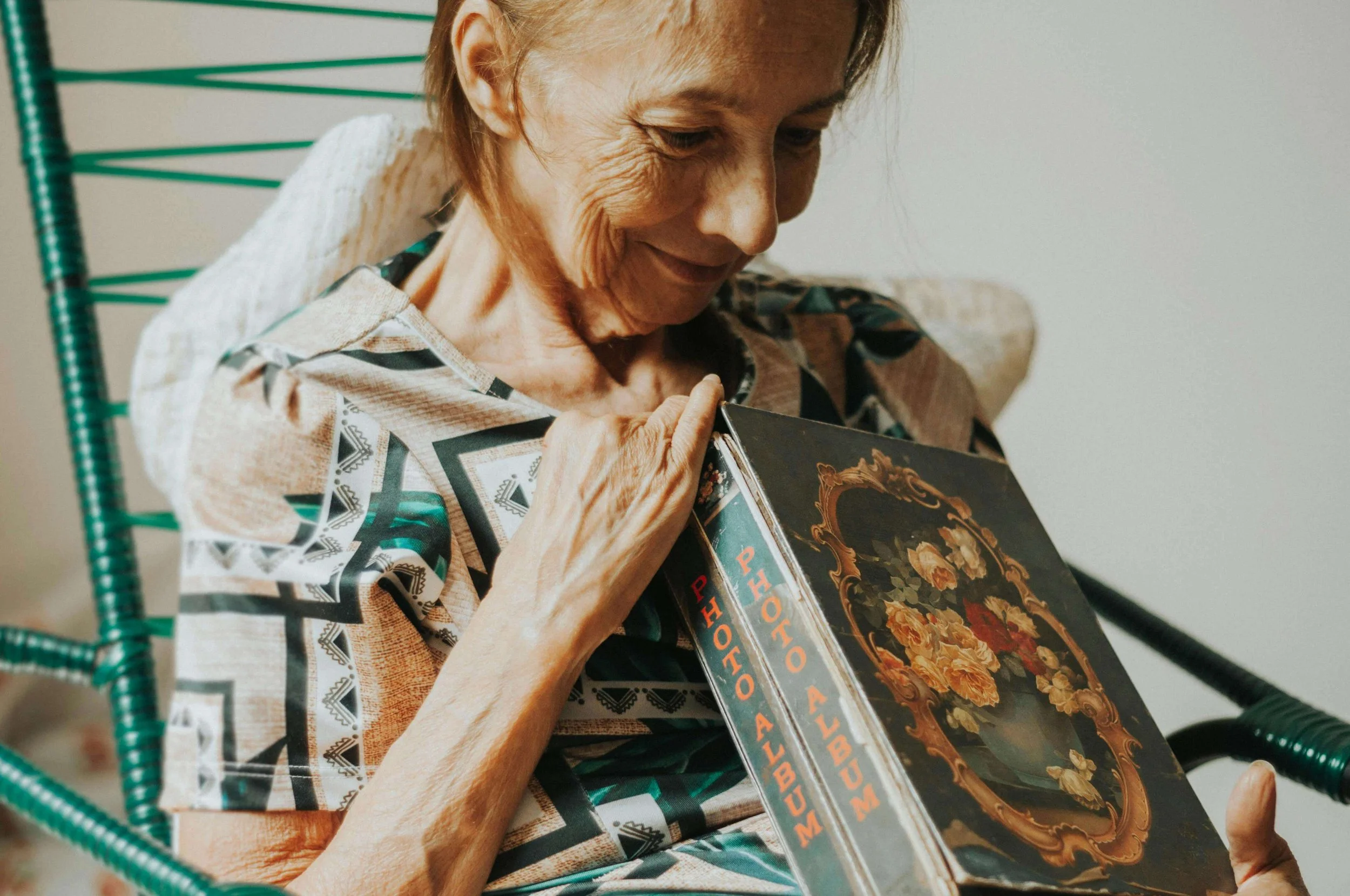 Older woman looking through a photo album with a soft expression, reflecting memory, continuity, and healing explored in childhood trauma therapy in Falls Church, VA.