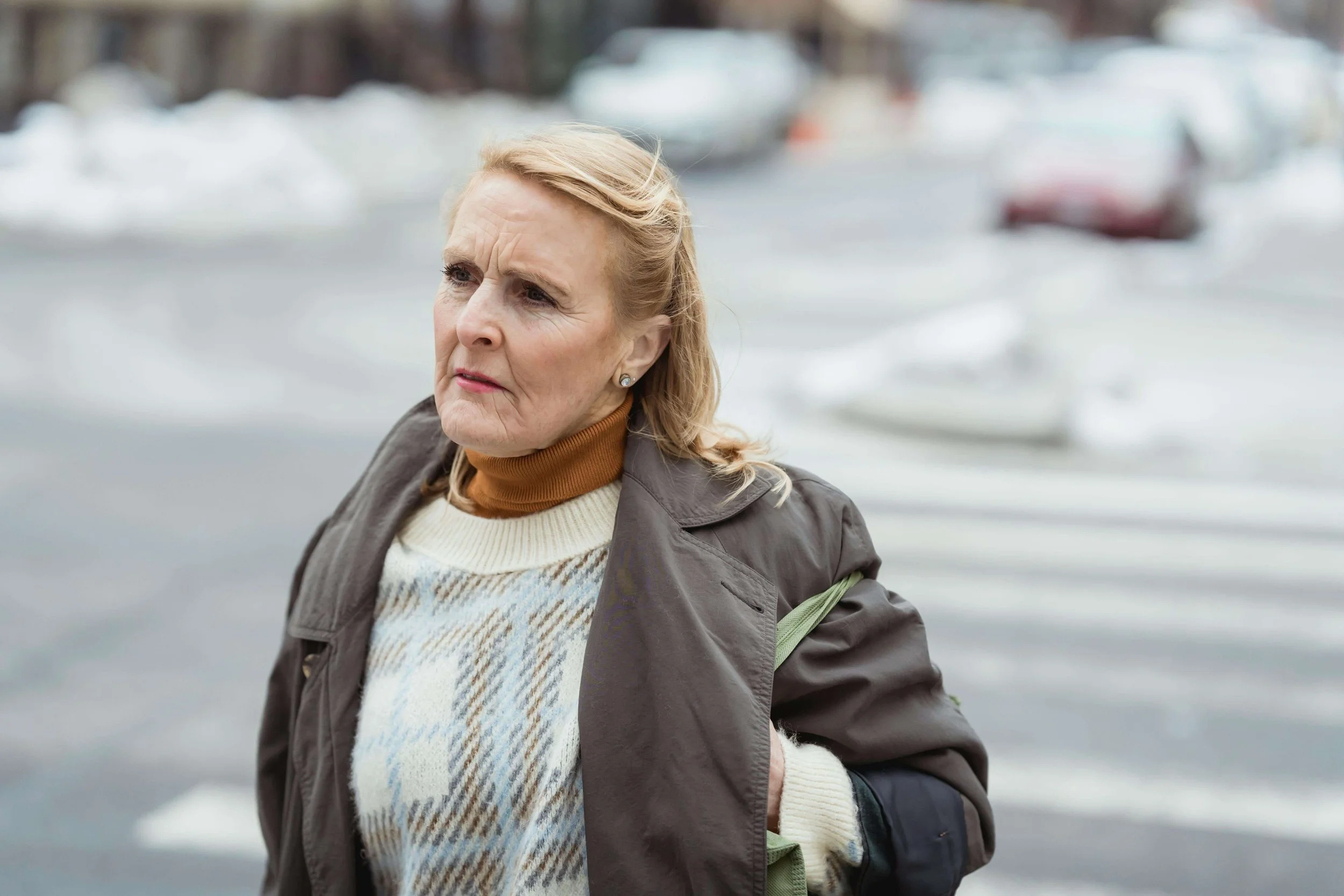 Woman walking across a street outdoors with wind blowing, appearing deep in thought, illustrating lived experiences addressed in emotional parentification trauma in Falls Church, VA.