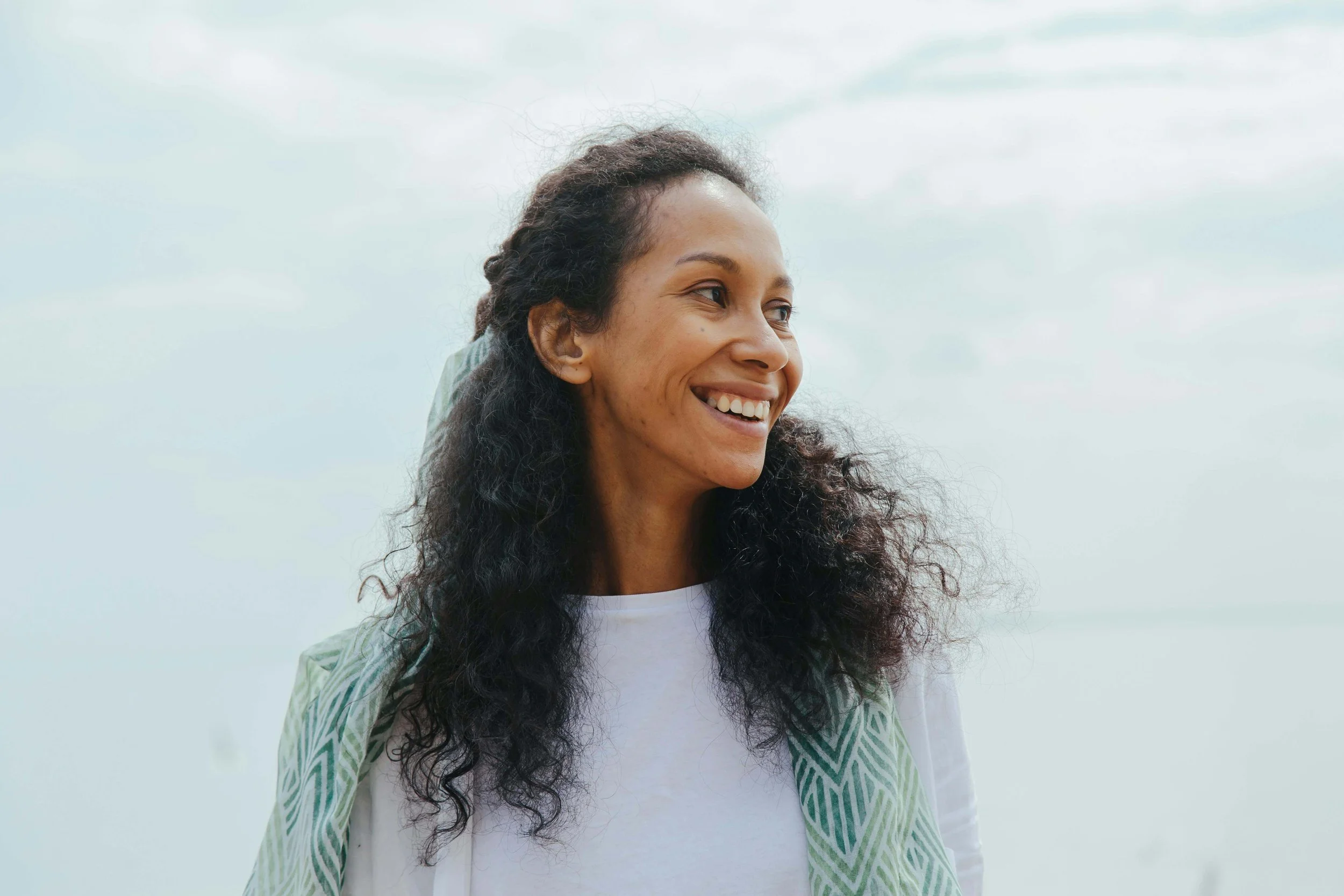 Woman smiling outdoors while looking to the side, symbolizing relief and self-acceptance through therapy for adult children of critical mothers in Falls Church, VA.