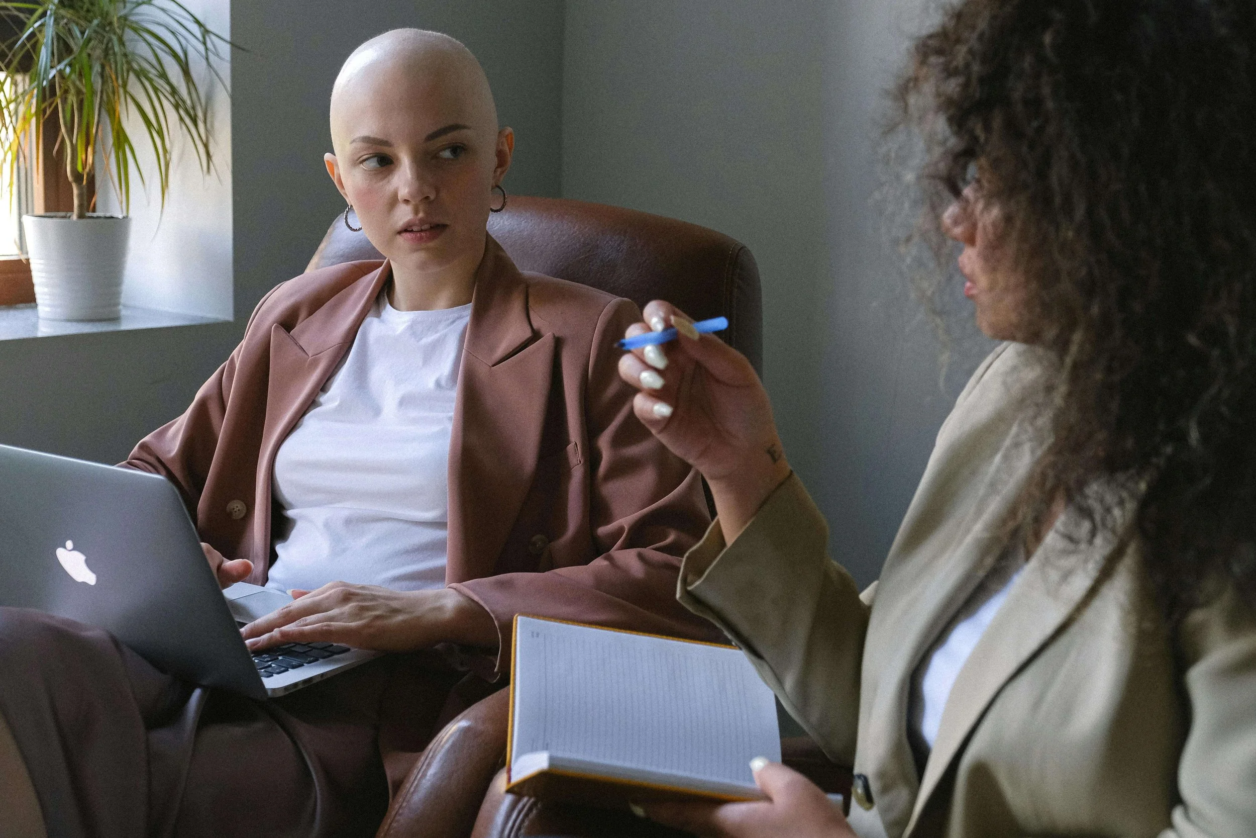 Bald woman in business attire appearing stressed at work with a colleague nearby, illustrating professional pressure and the need for trauma therapy for overthinking in Falls Church, VA.