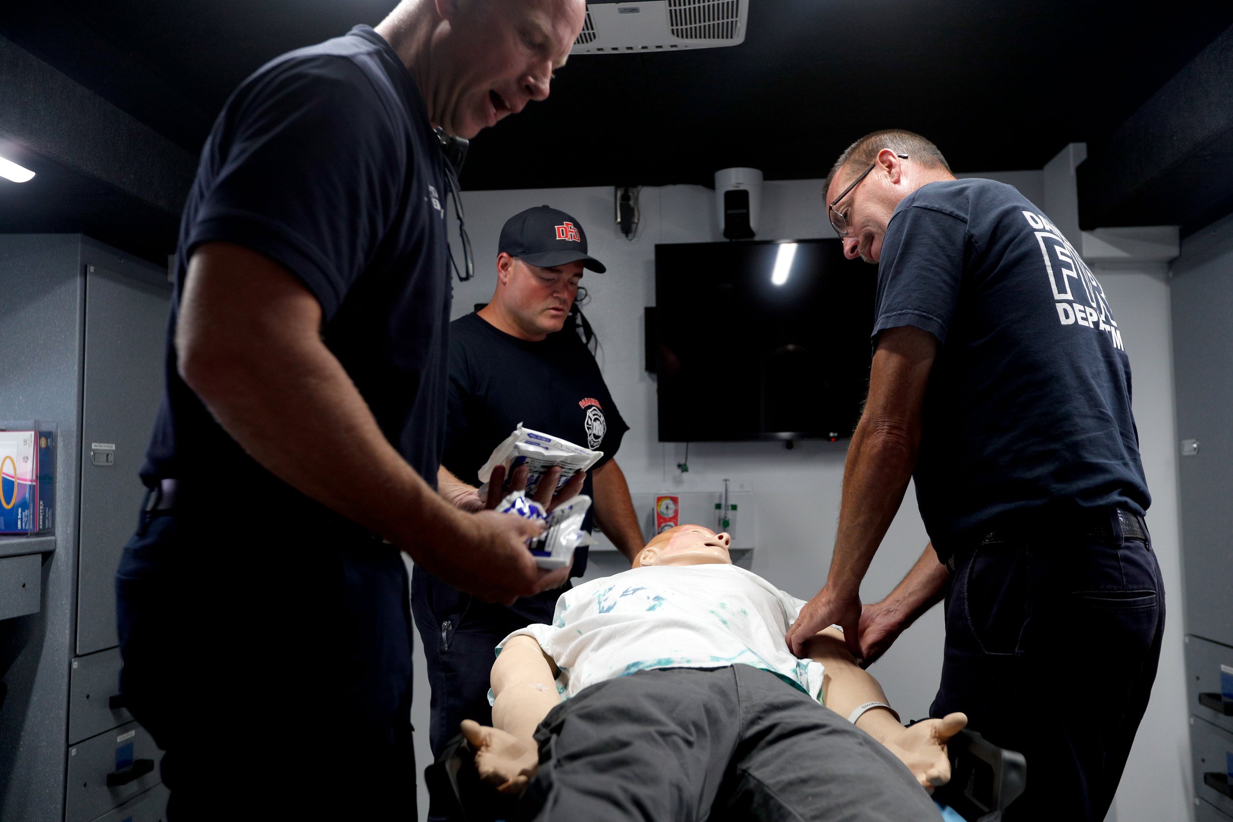Three emergency responders practicing CPR on a medical mannequin in a training room.